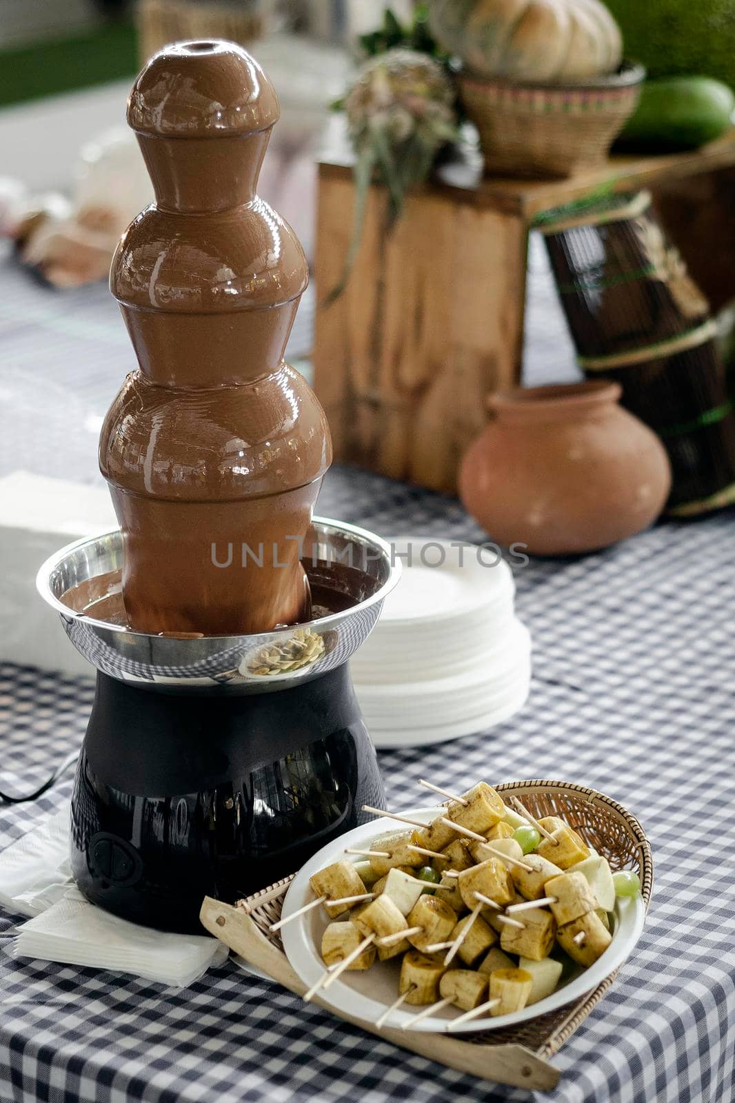 chocolate fountain catering machine with fruit skewers on rustic buffet table