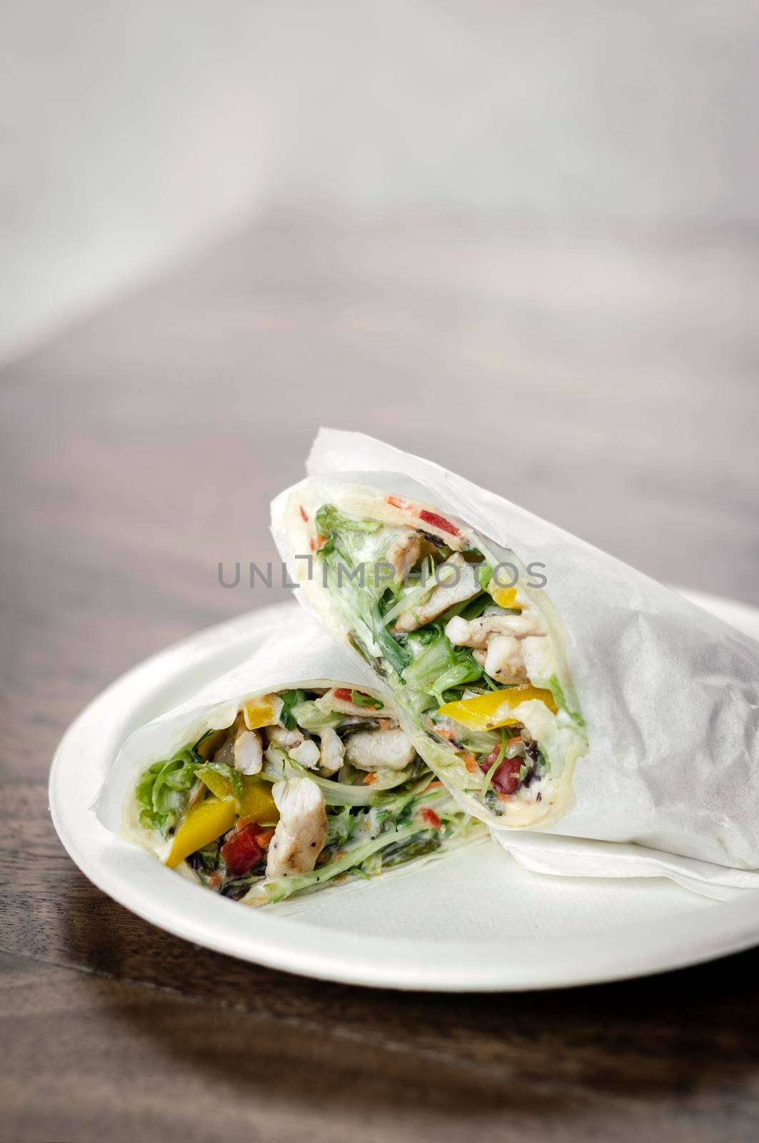 chicken salad wrap in white paper on wood table background by jackmalipan