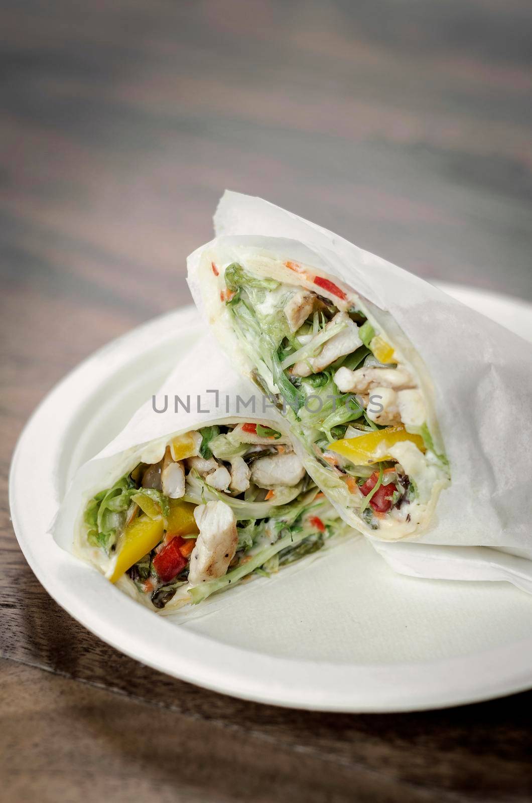 chicken salad wrap in white paper on wood table background by jackmalipan