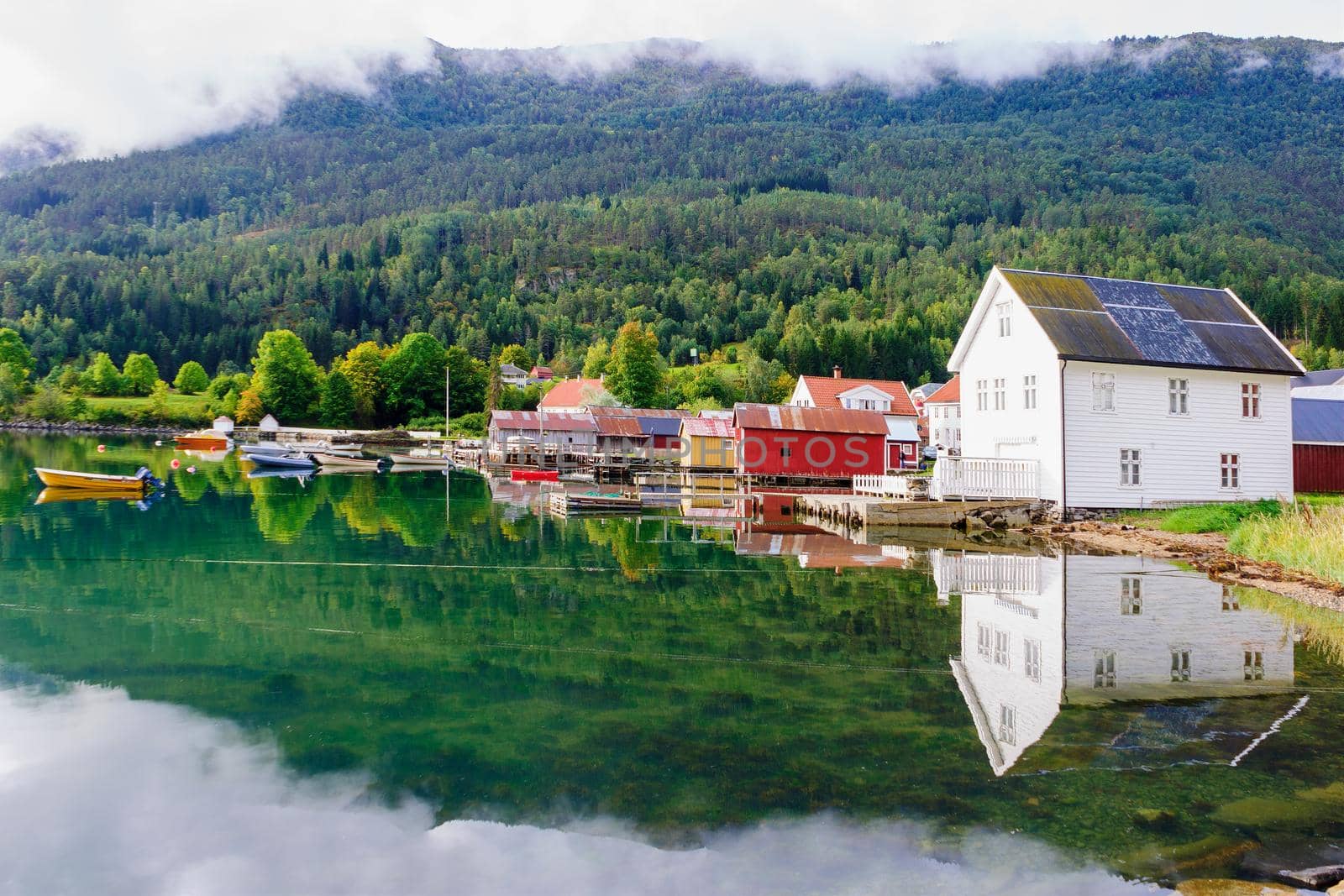 View of typical colorful houses, with boats, pier and reflection in Solvorn, Norway