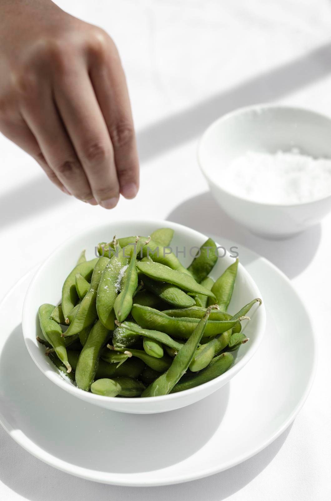 hand salting edamame beans snack in bowl on white restaurant table