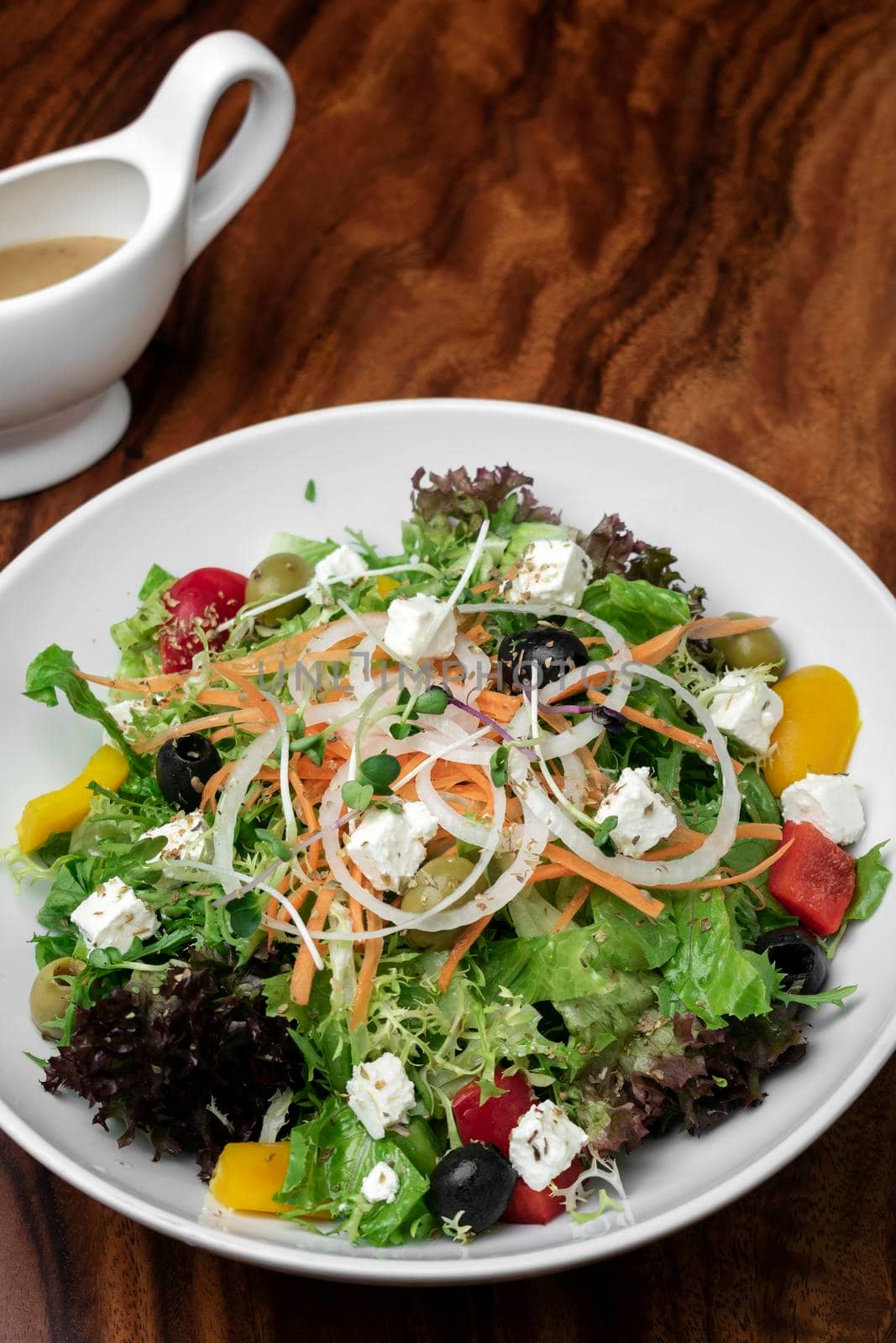 greek salad with feta cheese and olives with citrus vinaigrette on wooden table