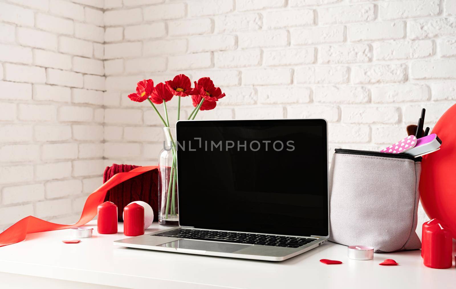 Valentines Day and Womens Day concept. laptop with cosmetic and spa accessories, gift box, flowers and candles on dressing table on white brick wall background