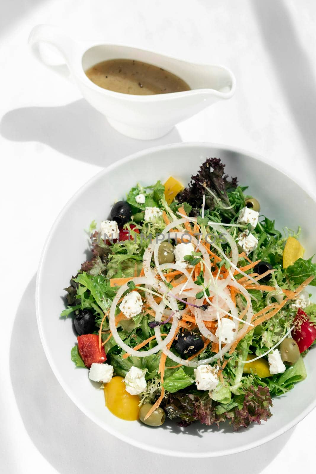 greek salad with feta cheese and olives with citrus vinaigrette on white table