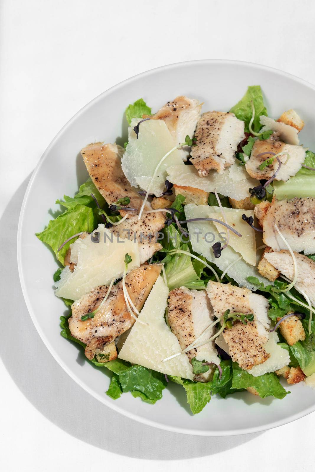 organic chicken caesar salad with parmesan cheese and croutons on white table background