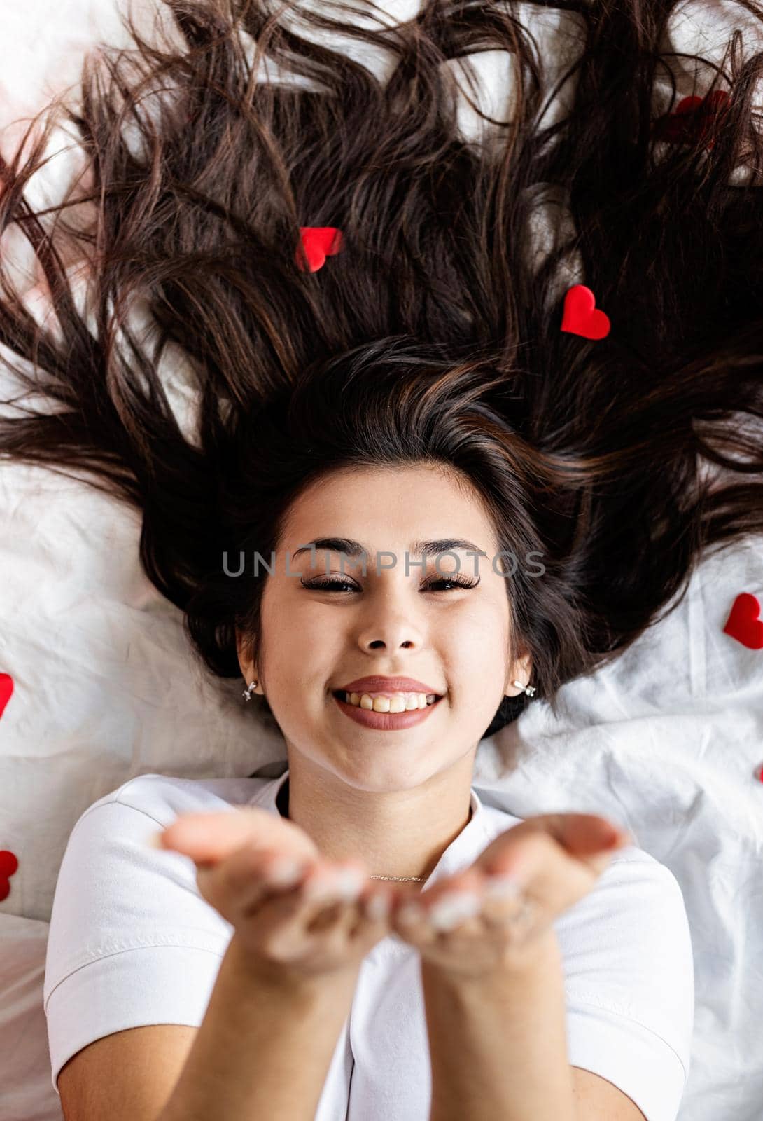 Valentines Day. Young happy brunette woman laying in the bed blowing a kiss