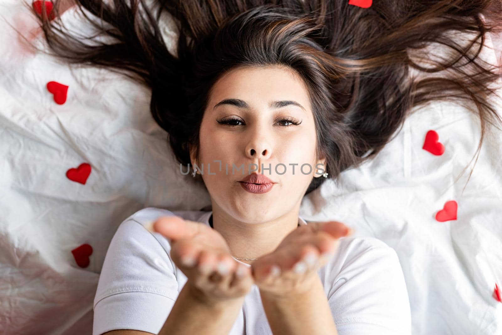 Valentines Day. Young happy brunette woman laying in the bed blowing a kiss
