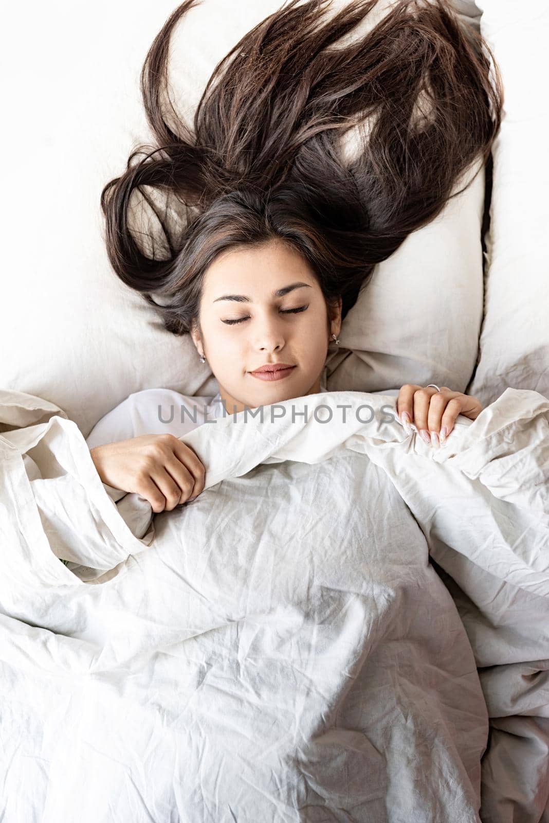 young beautiful brunette woman sleeping in bed covering her face with blanket