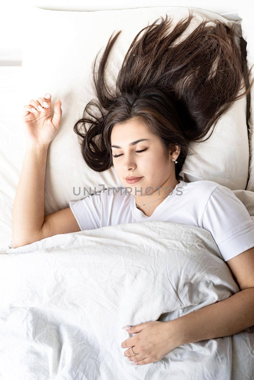 young beautiful brunette woman sleeping in bed covering her face with blanket