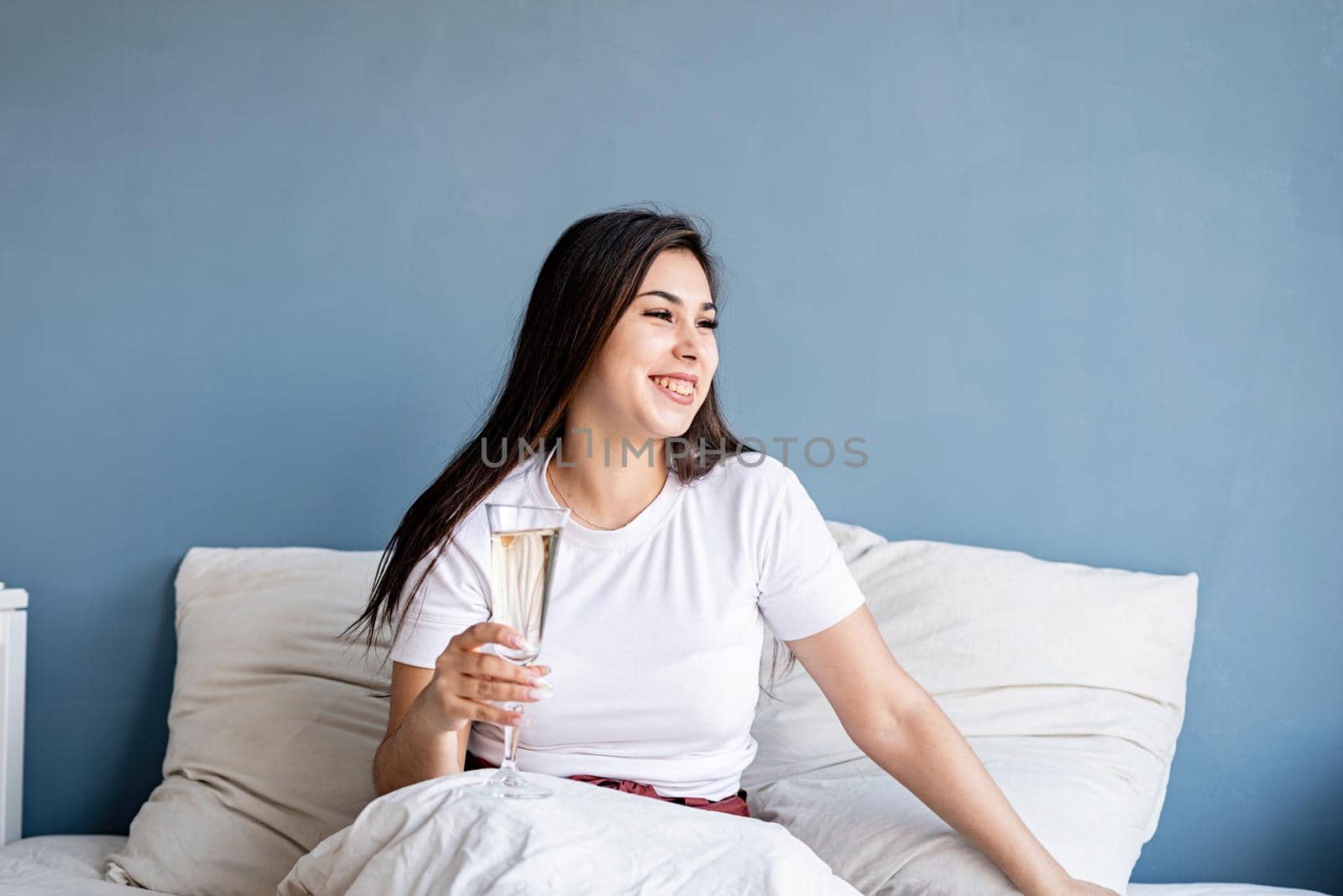Young brunette woman sitting awake in the bed drinking champagne by Desperada