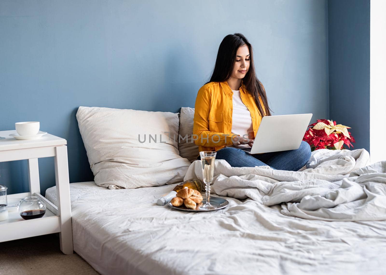 Young brunette woman sitting in the bed working on computer drinking champagne by Desperada