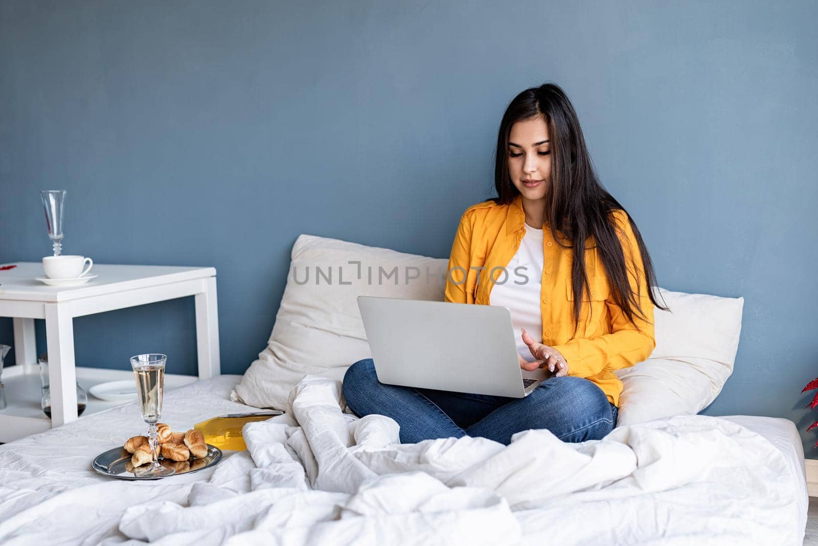 Young brunette woman sitting in the bed working on computer drinking champagne by Desperada