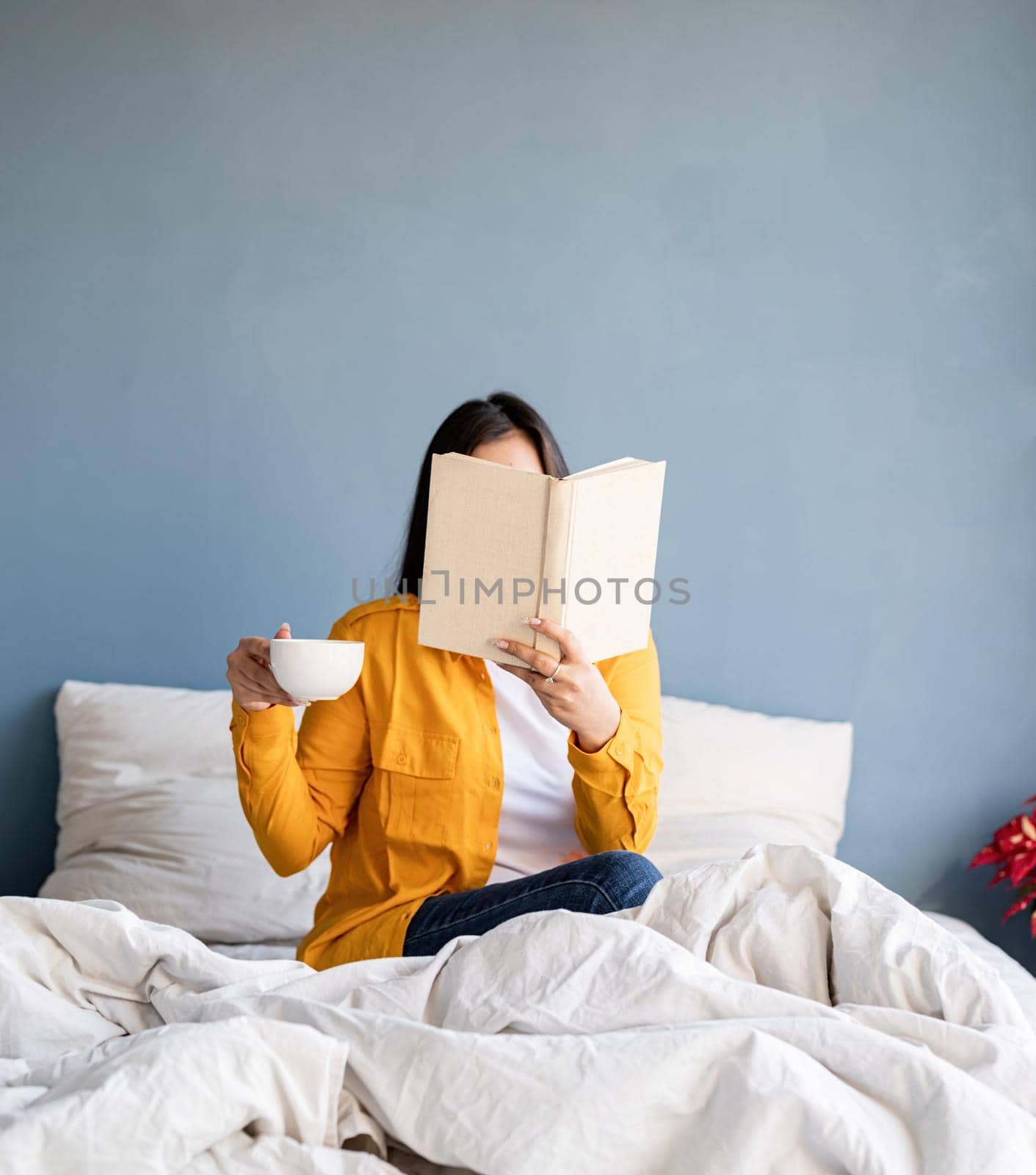 Young brunette woman sitting in the bed with eating croissants and reading a book by Desperada