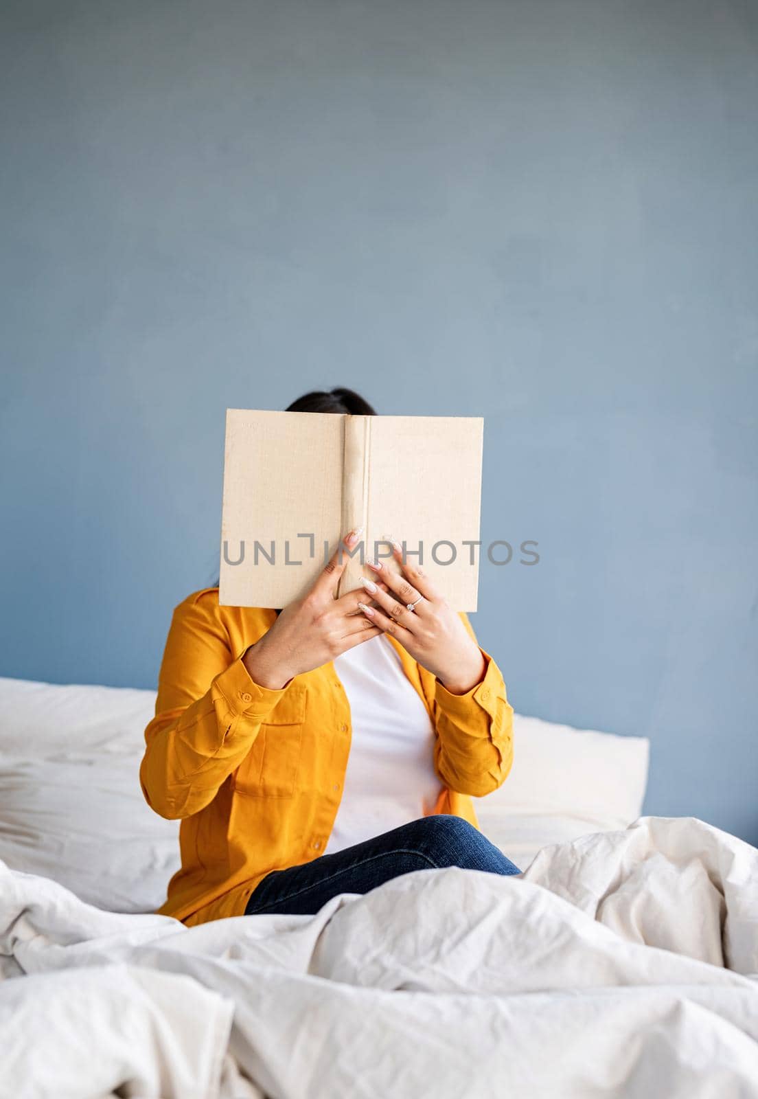 Young brunette woman sitting in the bed with eating croissants and reading a book by Desperada