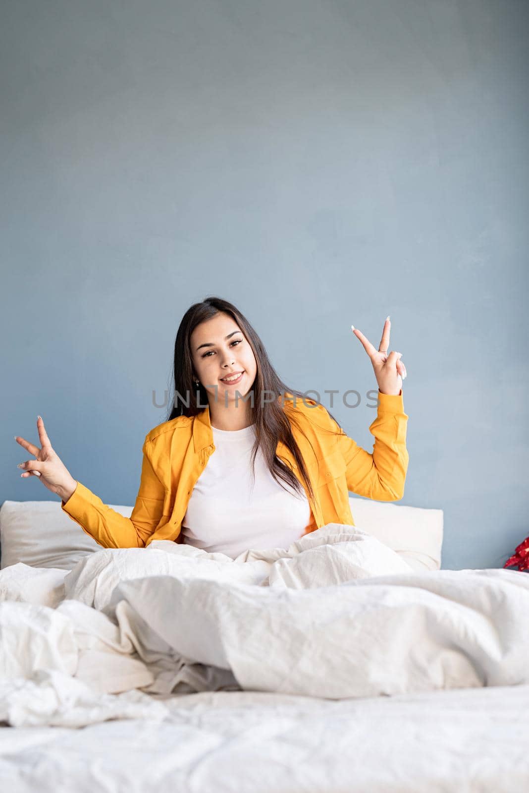 young beautiful brunette woman sitting awake in bed showing peace sign with her hands