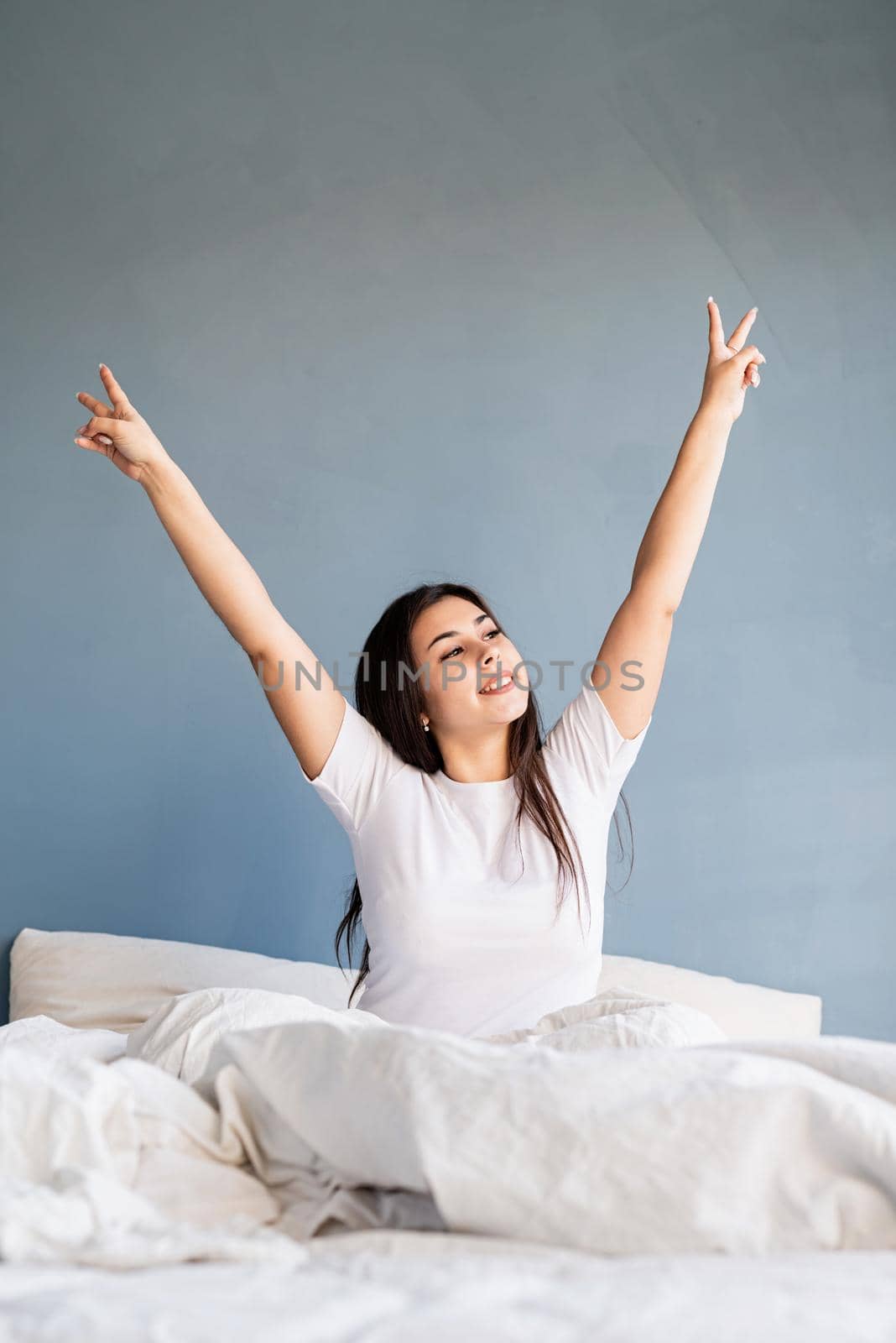 young beautiful brunette woman sitting awake in bed showing peace sign with her hands