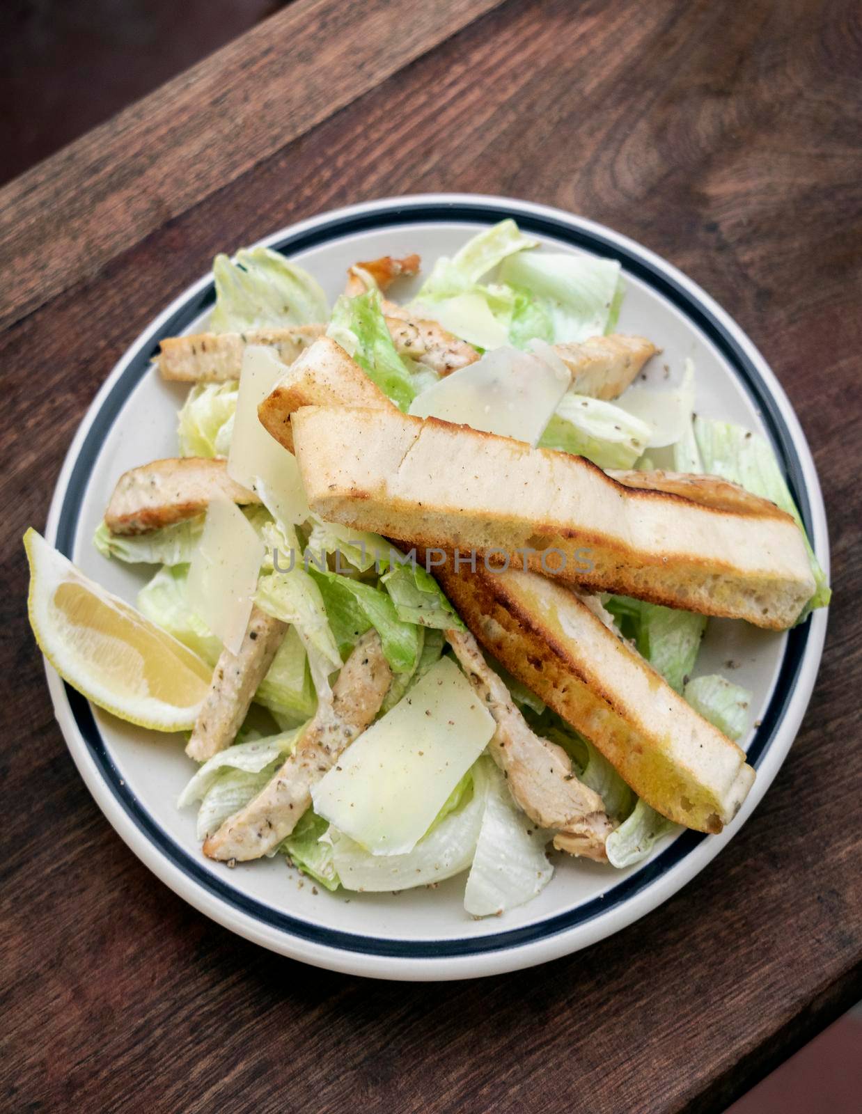 simple healthy chicken caesar salad on wood table  by jackmalipan