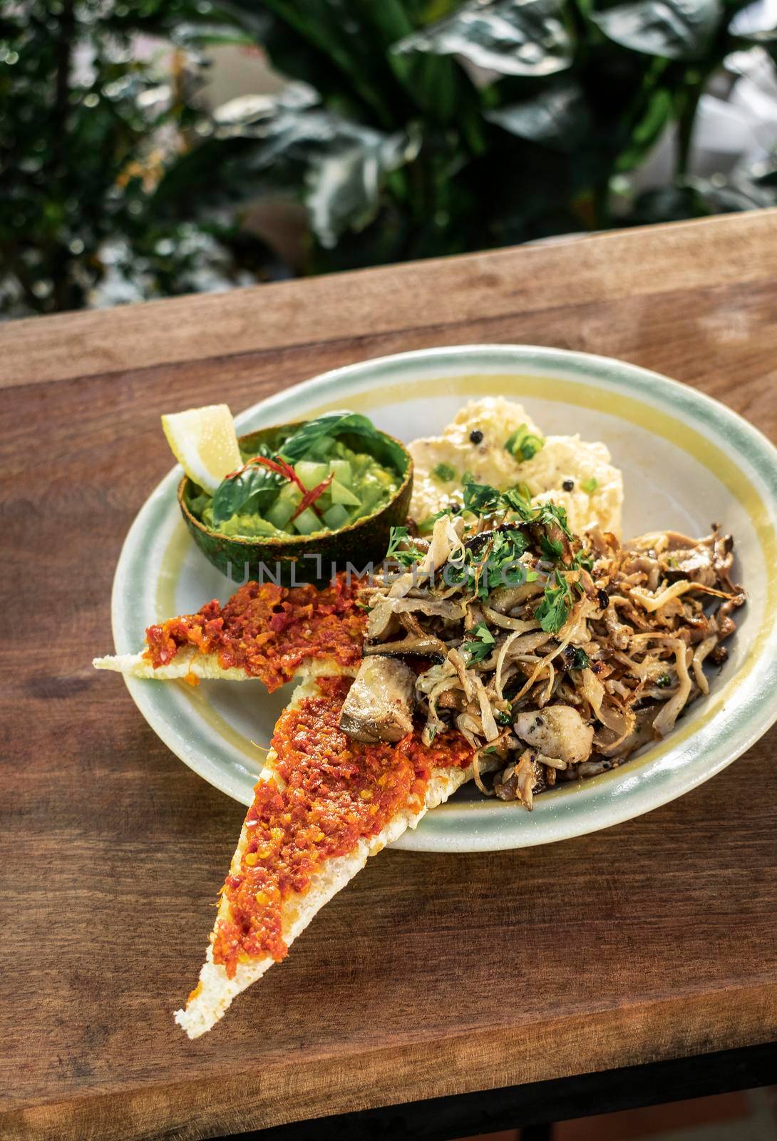 modern mexican brunch of fried mushrooms with guacamole and spicy red pepper paste toast and scrambled eggs