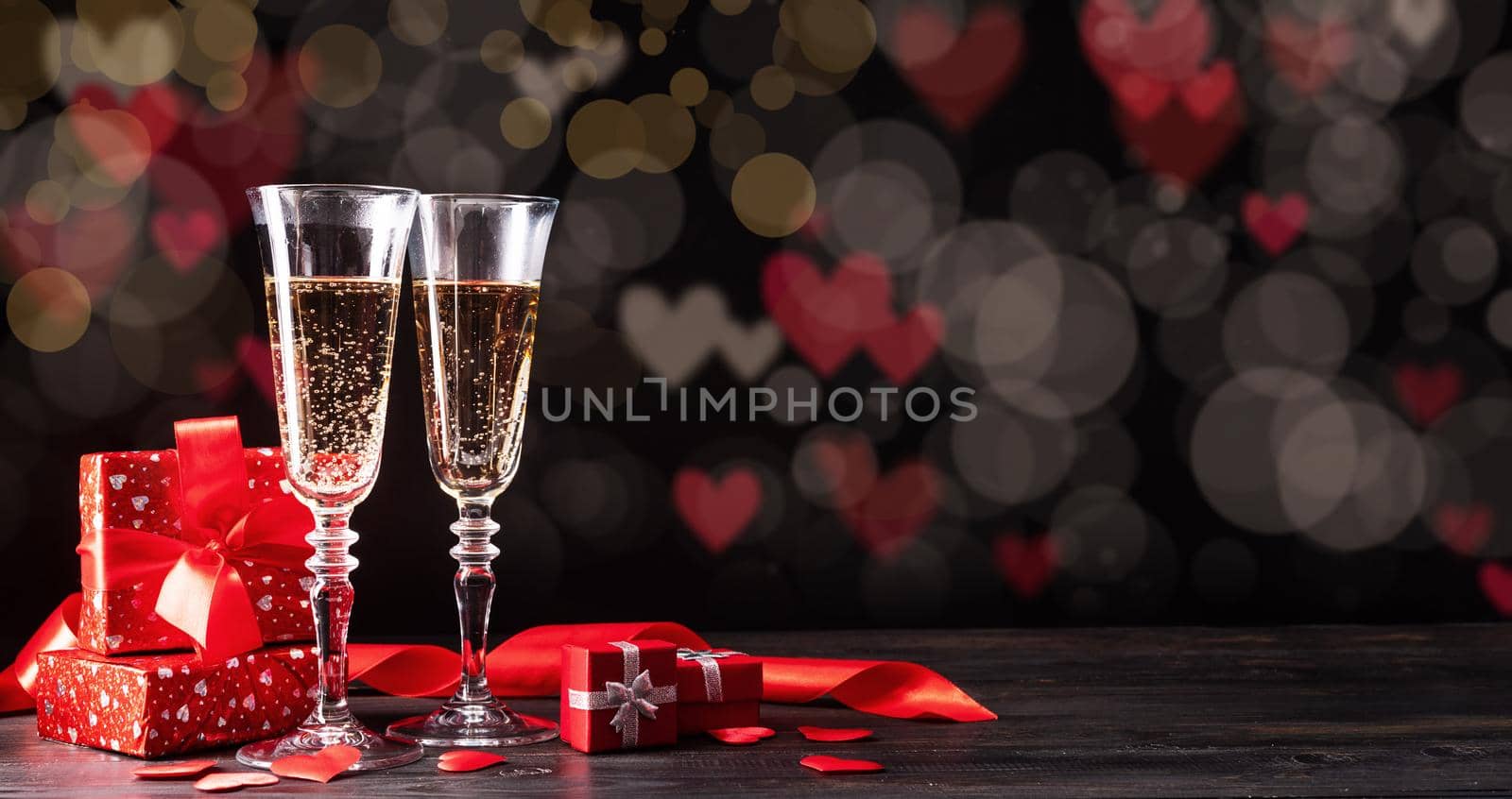 Valentines Day. Champagne flutes, candles and red hearts on beautiful bokeh background