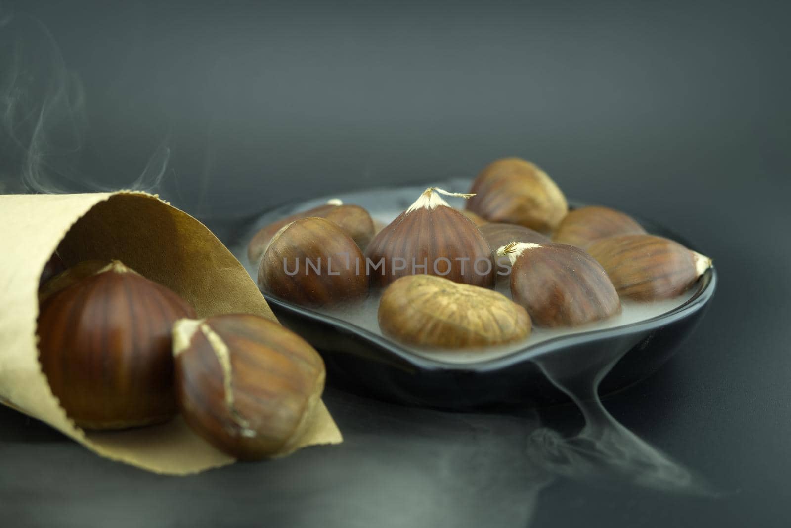 Roasting chestnuts in a black pan, surrounded by white smoke and a cone-shaped paper cone, a dish for a traditional healthy winter snack or appetizer
