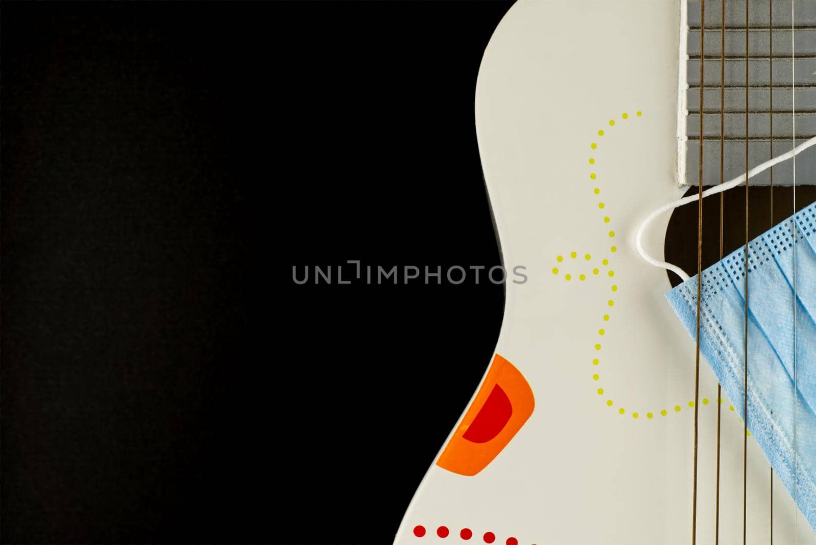 Wooden acoustic guitar body and a face mask between the strings over a black background with free space for text