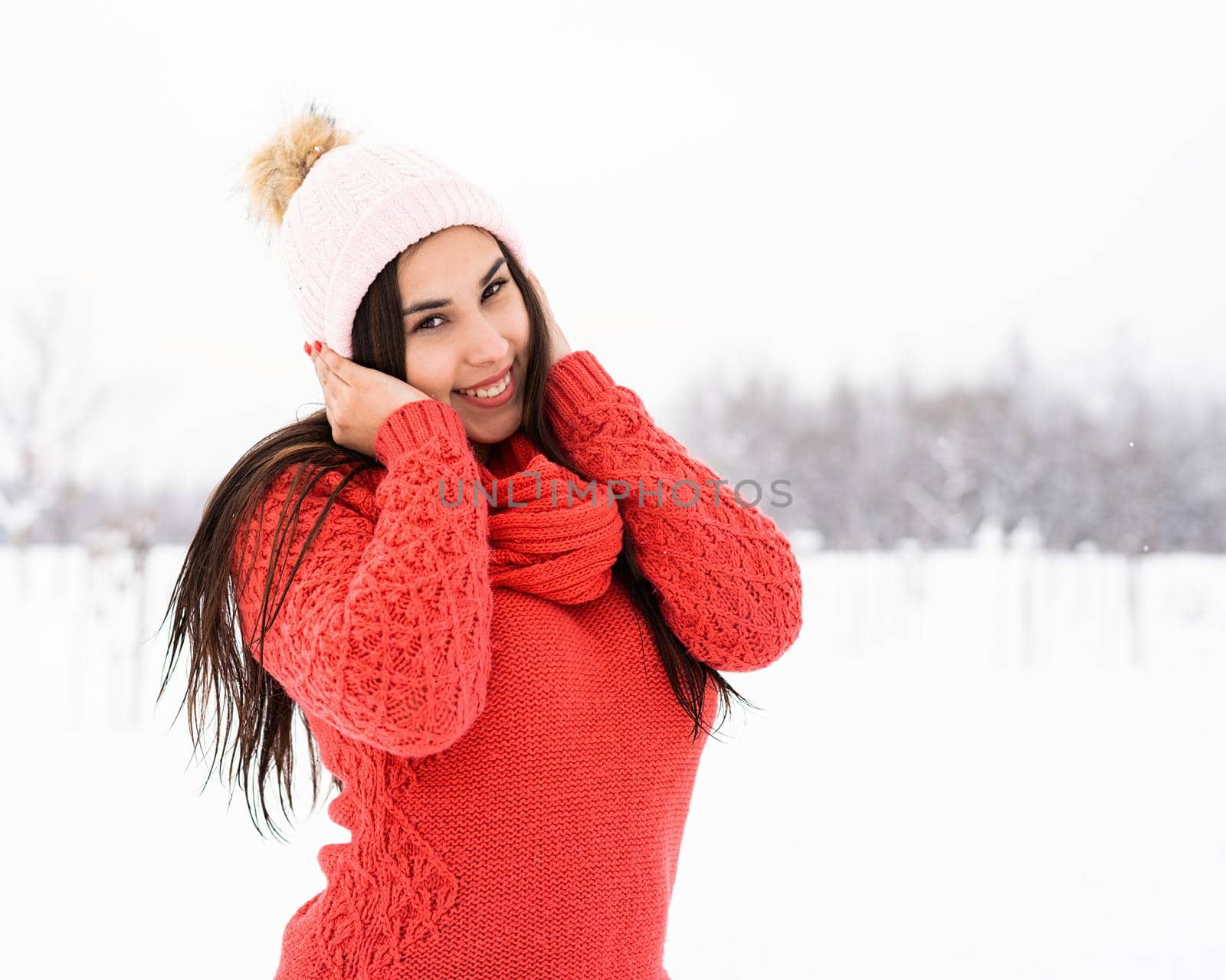 Winter season. Portrait of a beautiful smiling woman in red sweater and hat in snowy park