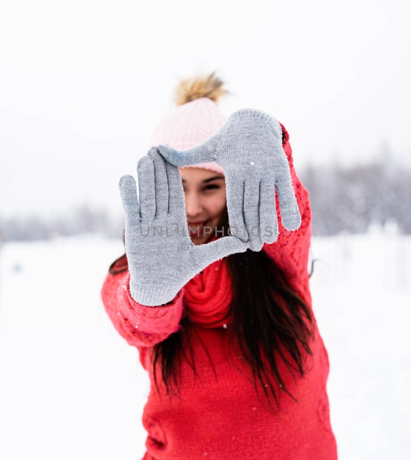 Winter season. beautiful young woman in red sweater making frame sign with her hands outdoors in snowy day