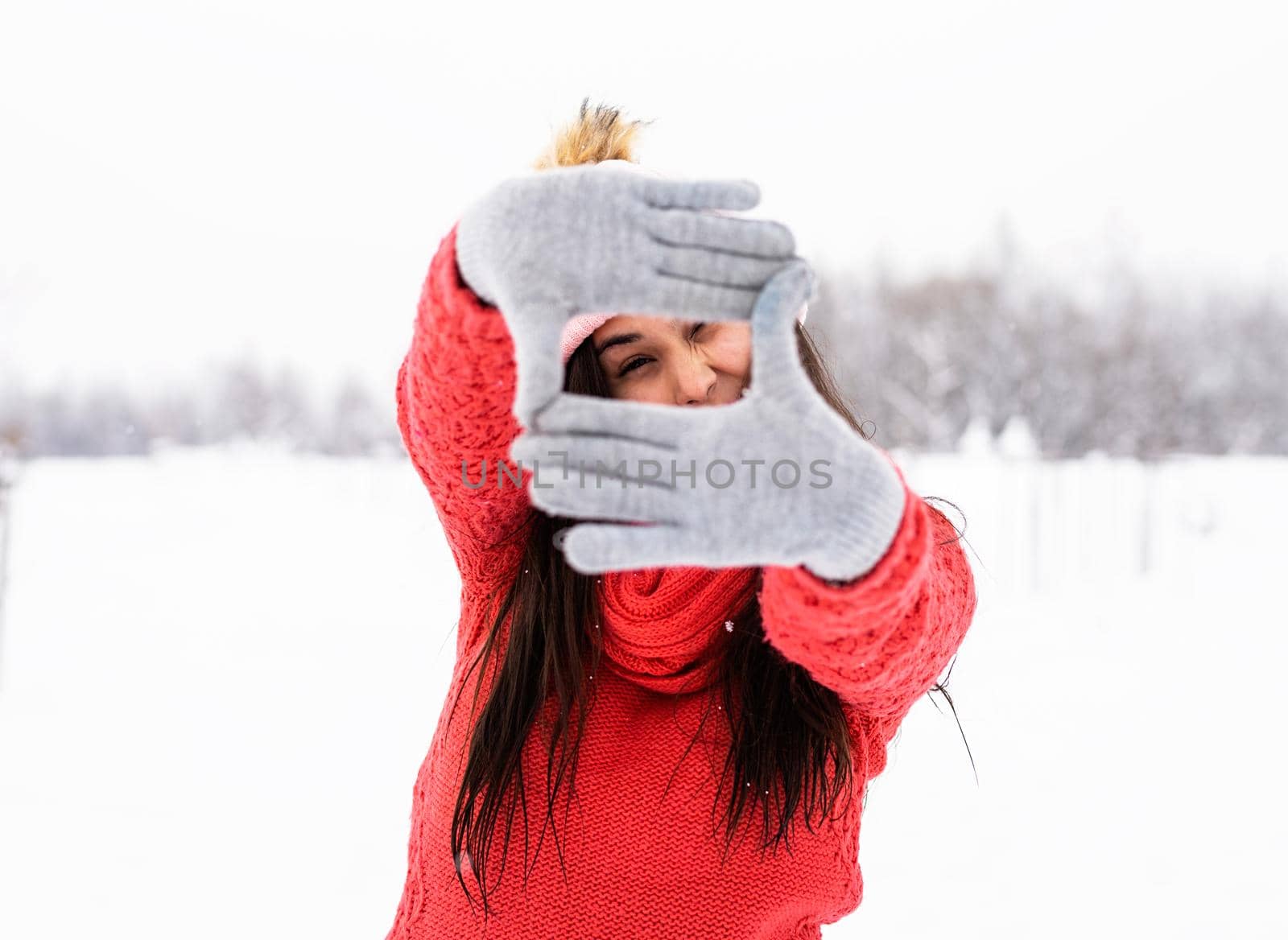 beautiful young woman in red sweater making frame sign with her hands outdoors in snowy day by Desperada