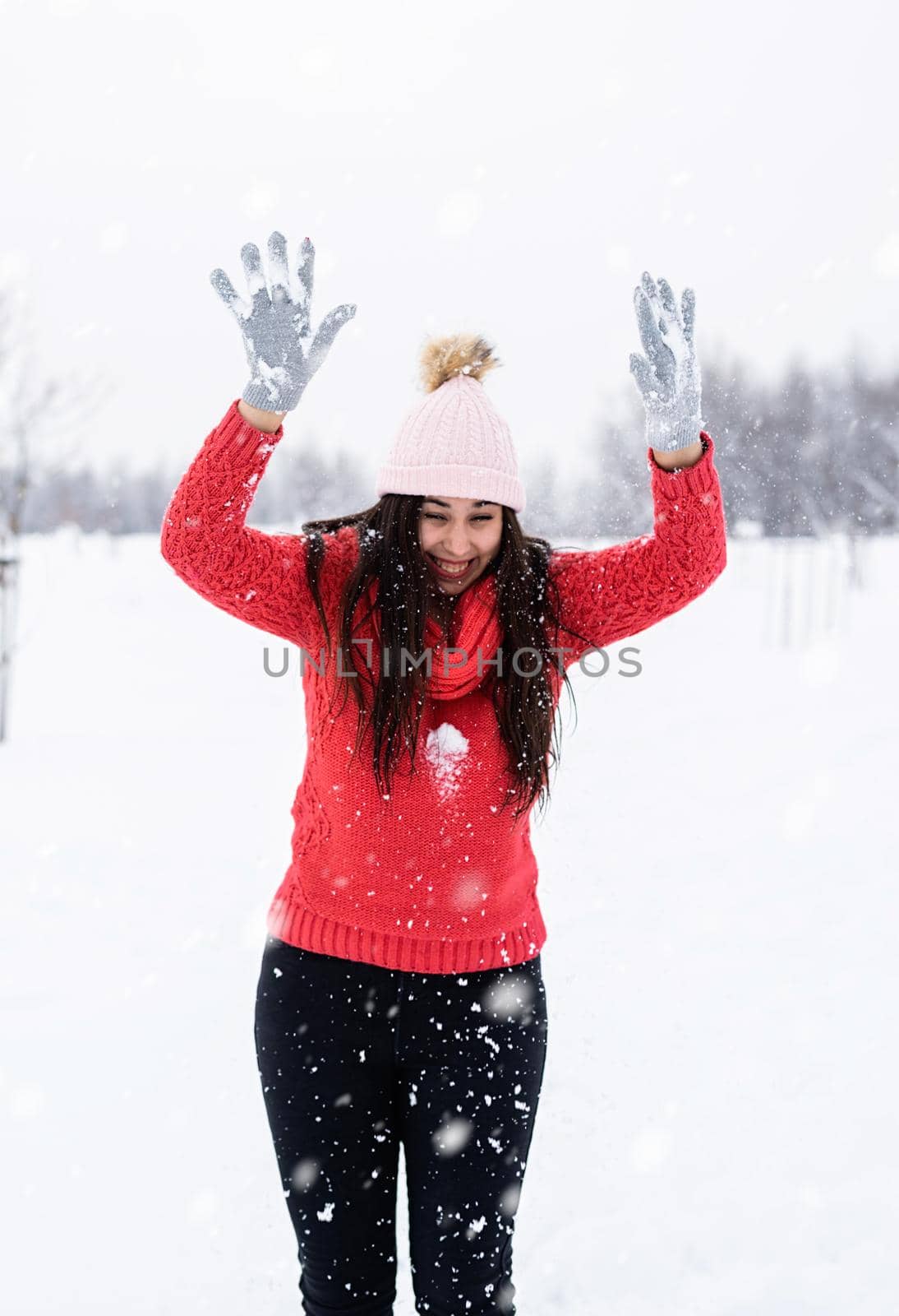 Young brunette woman in red sweater playing with snow in park by Desperada