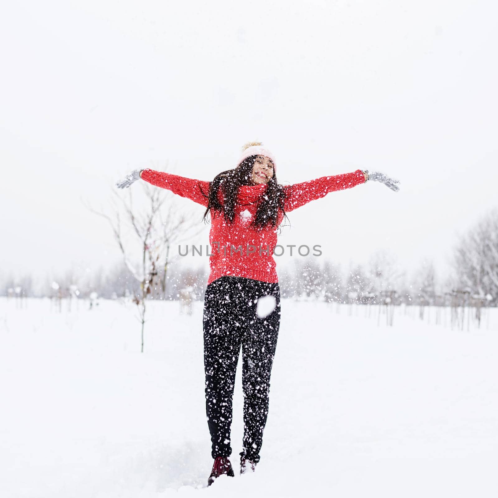 Young brunette woman in red sweater playing with snow in park by Desperada