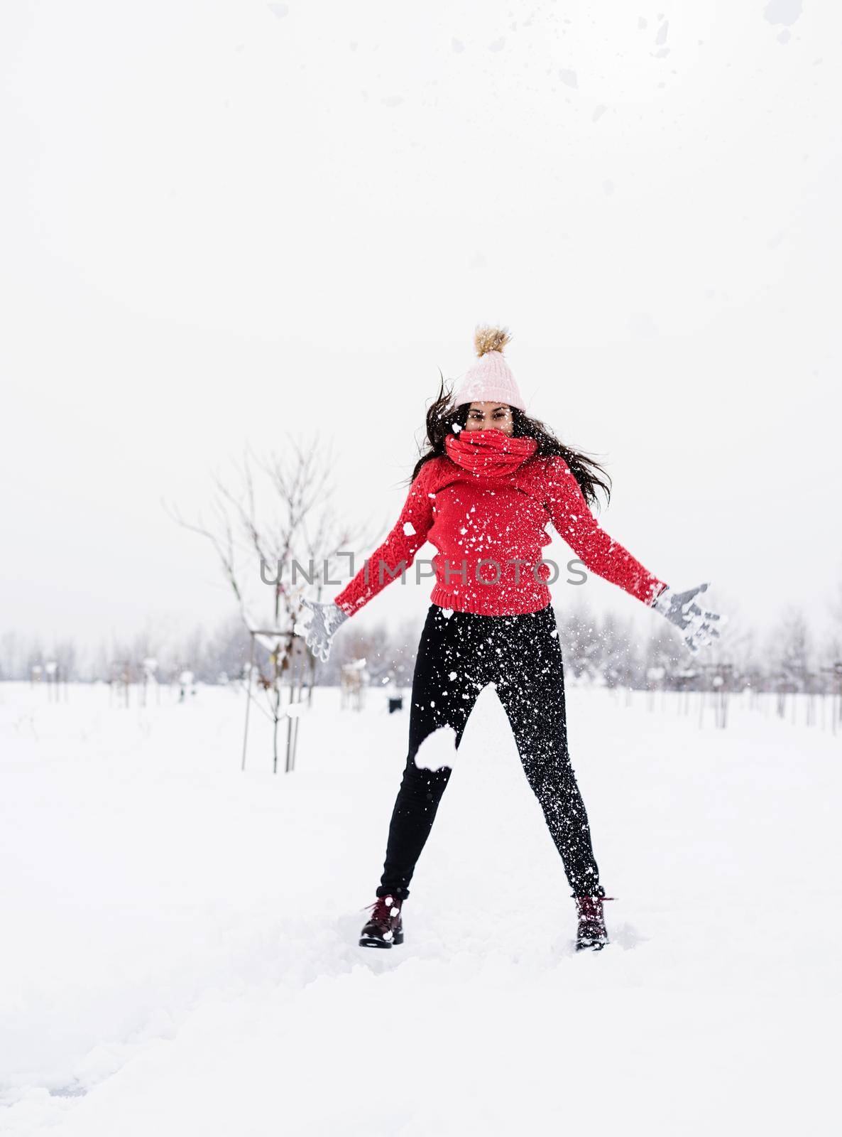 Young brunette carefree woman in red sweater jumping in snow outdoors by Desperada