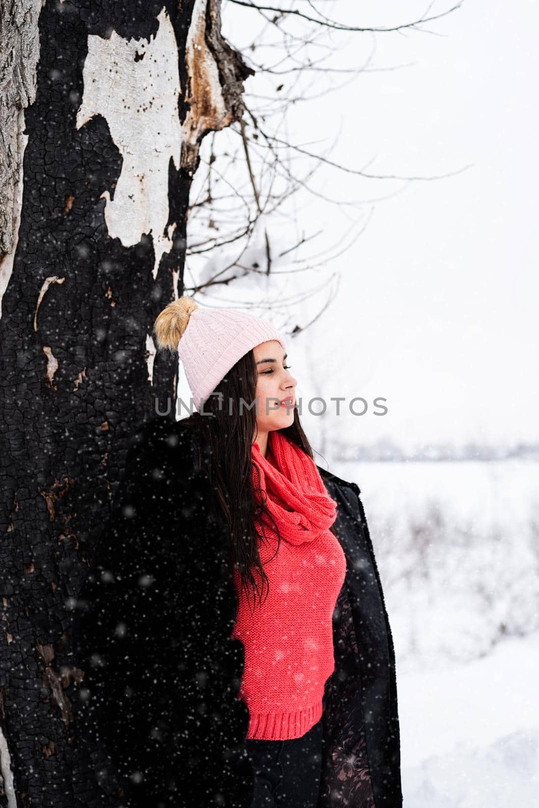 Portrait of a beautiful smiling young woman standing by the tree in snowfall by Desperada