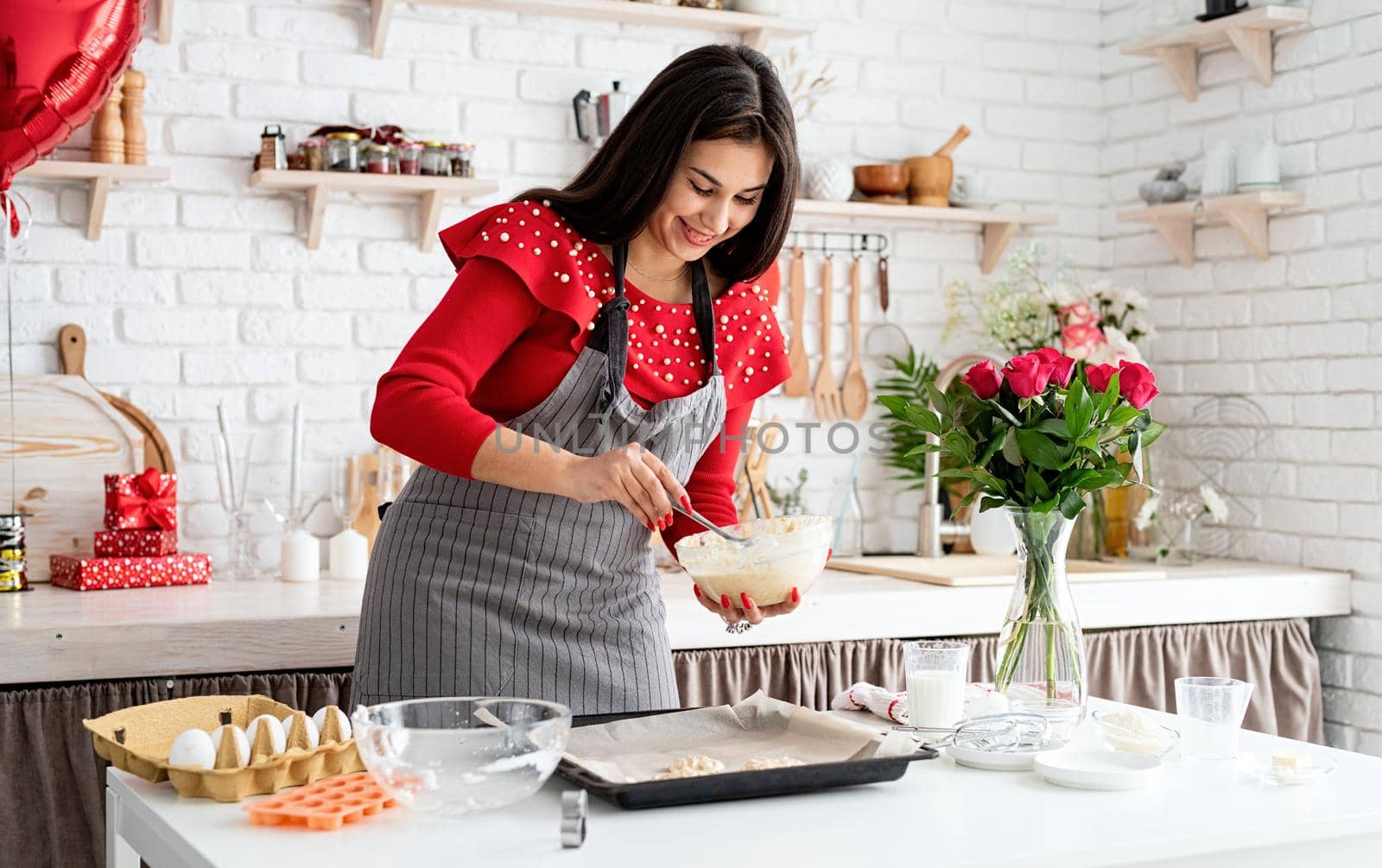 Woman in red dress and gray apron making valentine cookies at the kitchen by Desperada