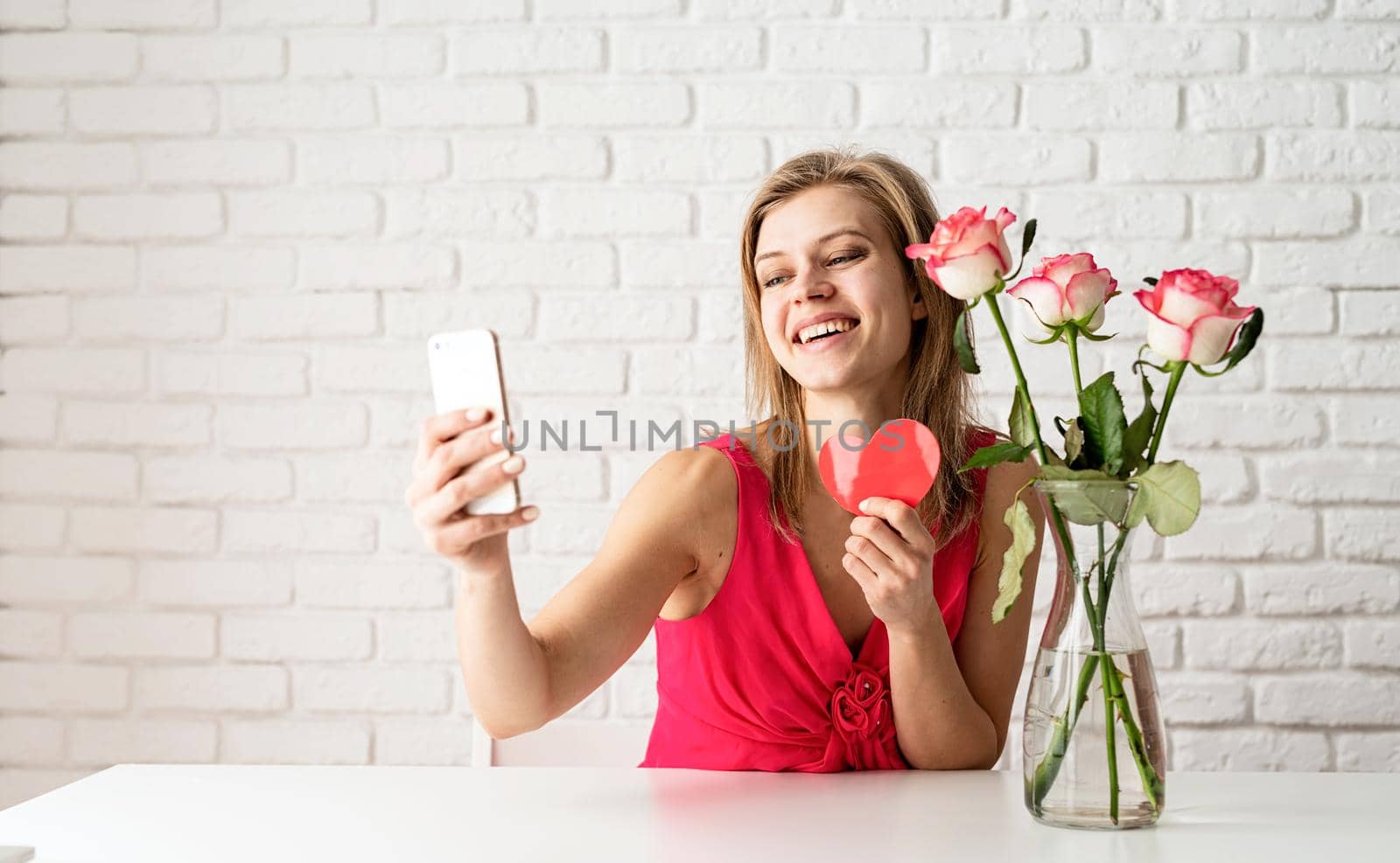 Valentines Day. Beautiful woman in pink dress dating online holding a heart in her hands