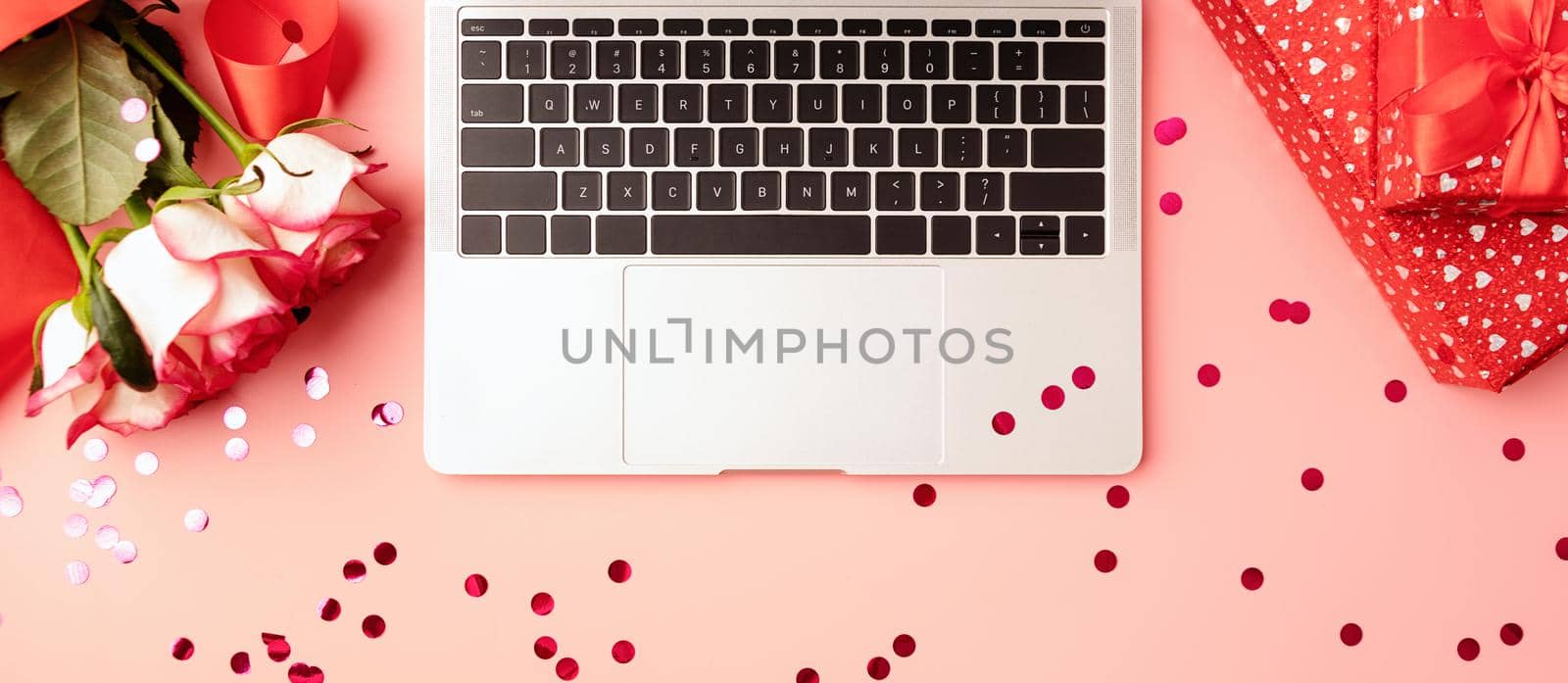 Valentines Day concept. Top view of valentines day workspace with laptop keyboard, confetti, flowers and gift boxes