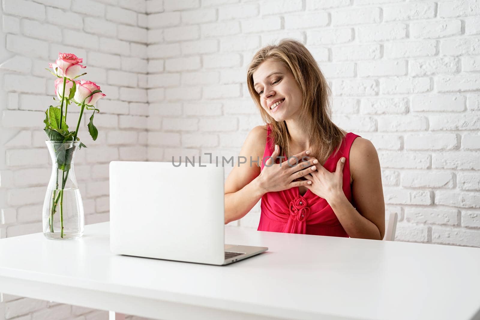 Valentines Day. Happy young woman in pink dress dating online touching heart with her hands