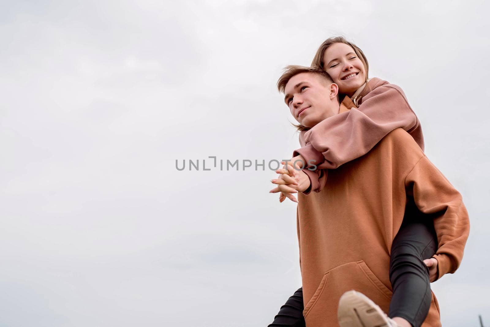 Happy young loving couple wearing hoods embracing each other outdoors in the park having fun on sky background