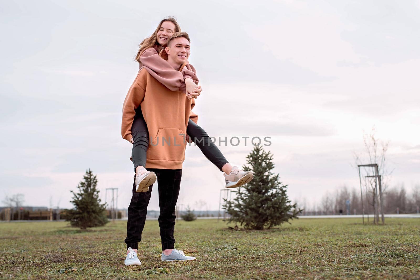 Happy young loving couple wearing hoods embracing each other outdoors in the park having fun