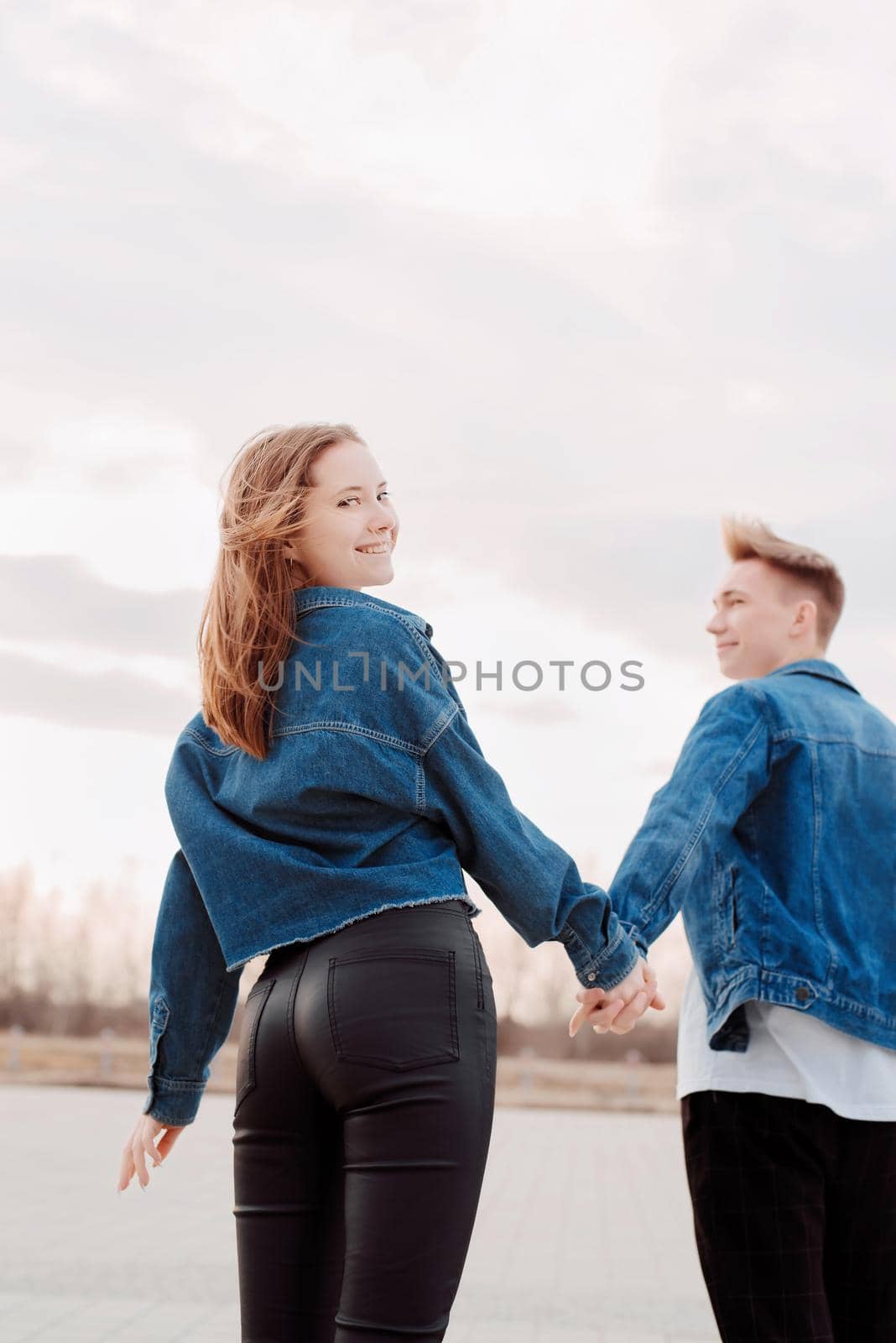 Young loving couple wearing jeans spending time together in the park having fun, woman holding hands with her boyfriend looking back