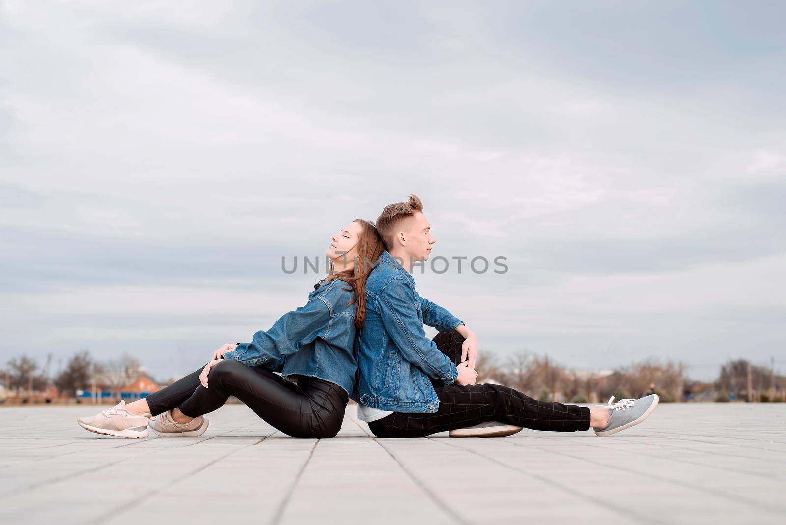 Young loving couple wearing jeans sitting back to back in the street spending time together