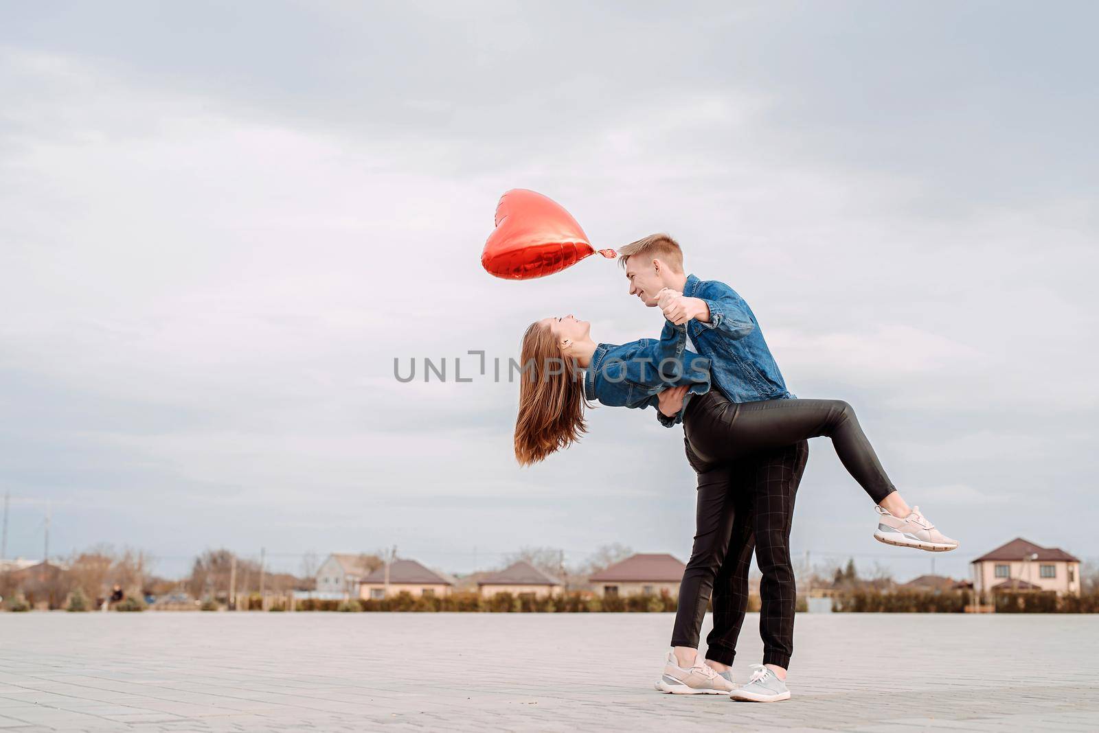 Valentines Day. Young couple dancing passionate tango on the square in the park holding red balloon