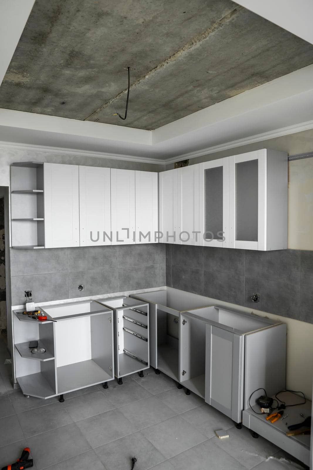 Custom kitchen cabinets installation with a white furniture facades mdf. Gray modular kitchen from chipboard material on a various stages of installation. A frame furniture fronts mdf profile