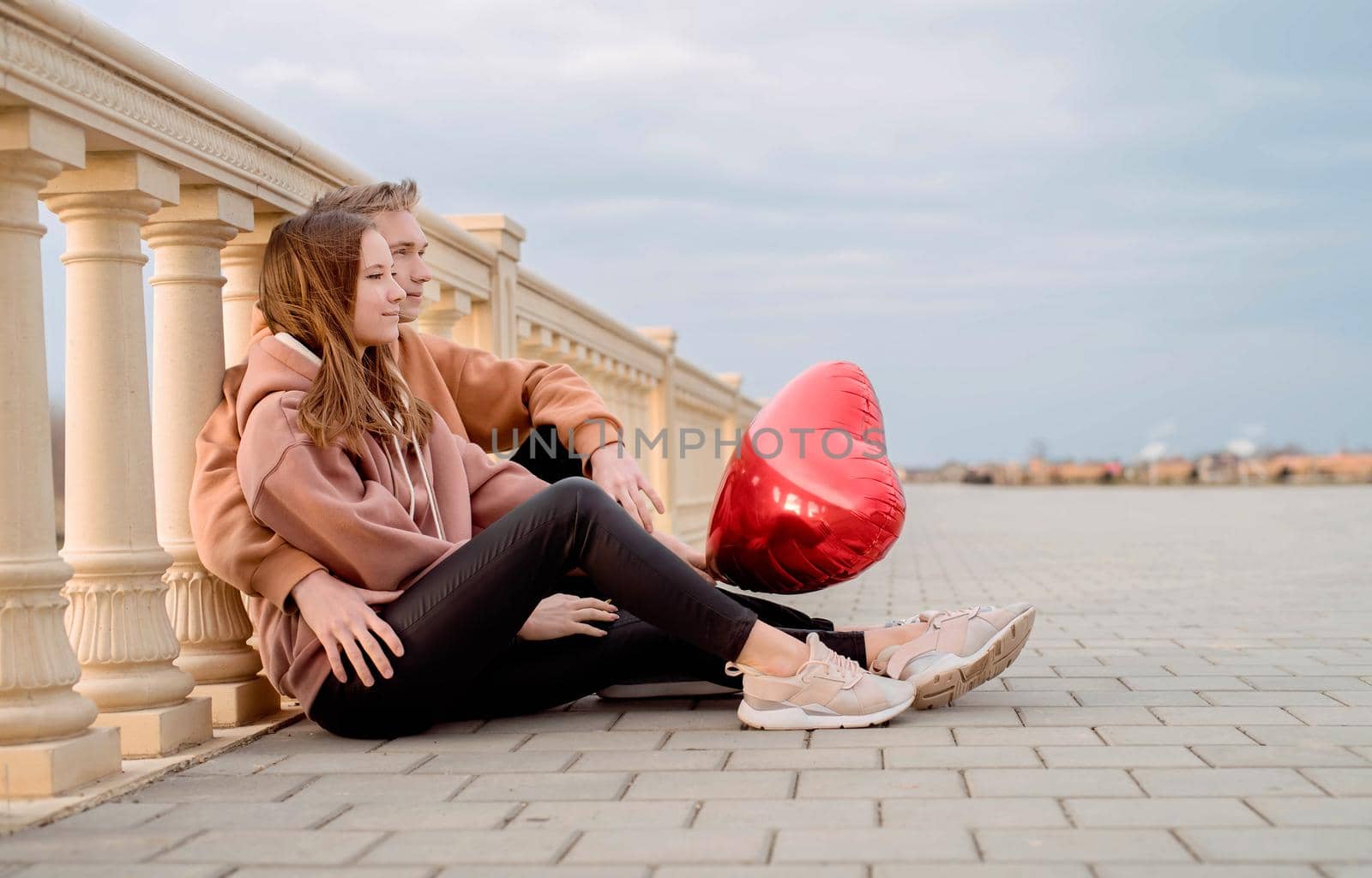 Happy young loving couple embracing each other outdoors in the park having fun holding red balloons