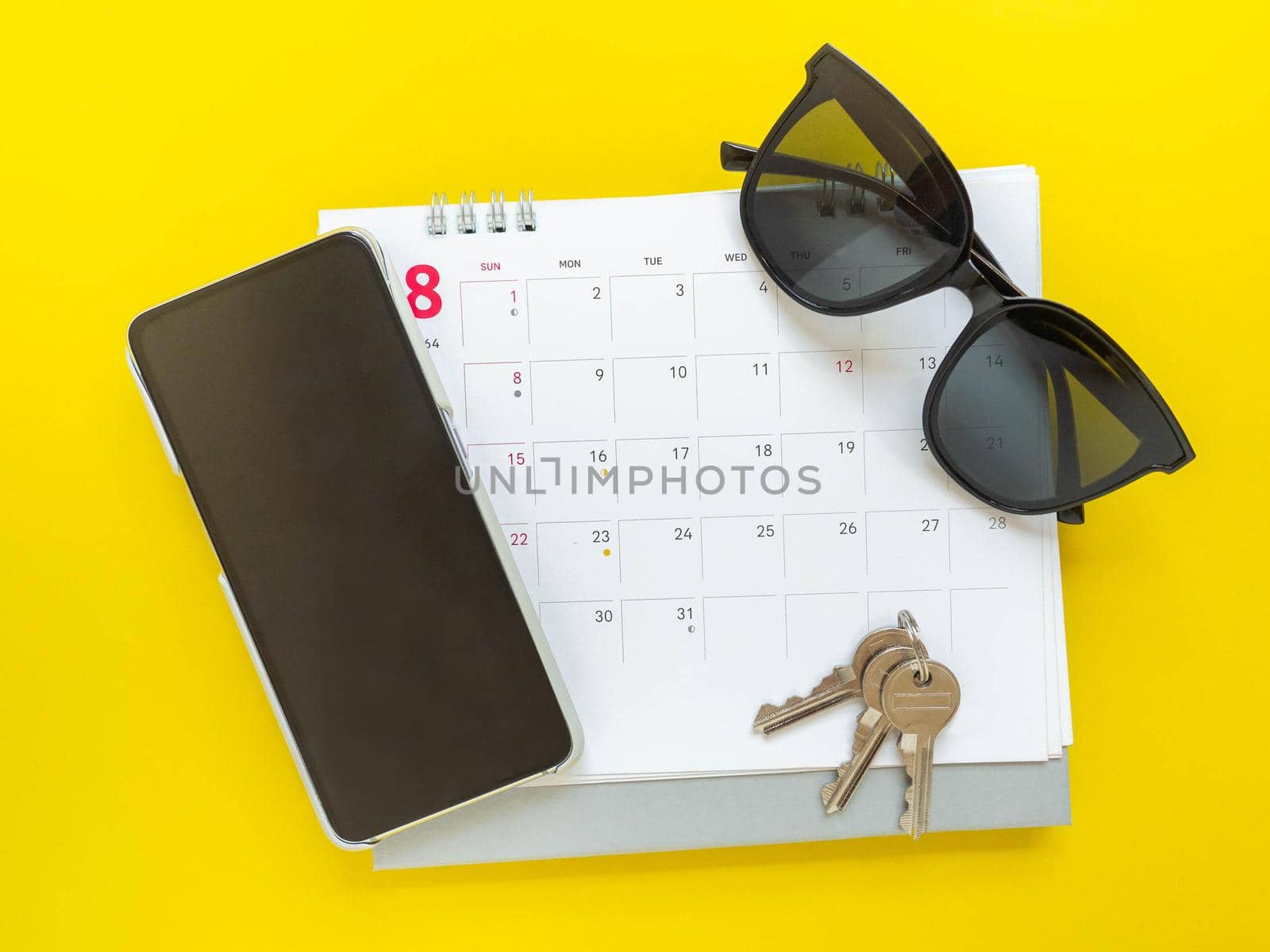 Dark glasses, keys, cell phone, and calendar prepare for departure.