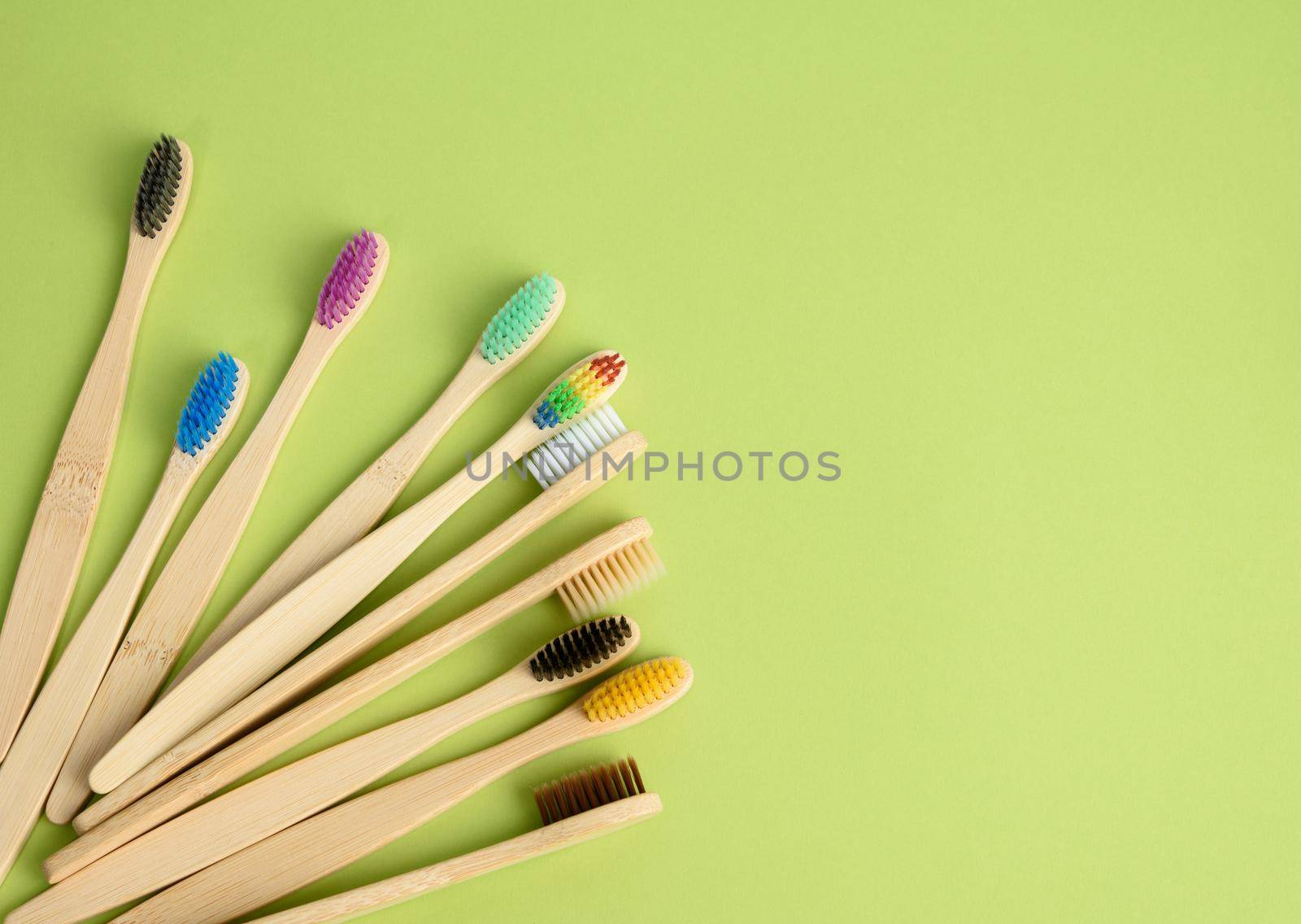 multicolored wooden toothbrushes on a green background, plastic rejection concept, zero waste, top view