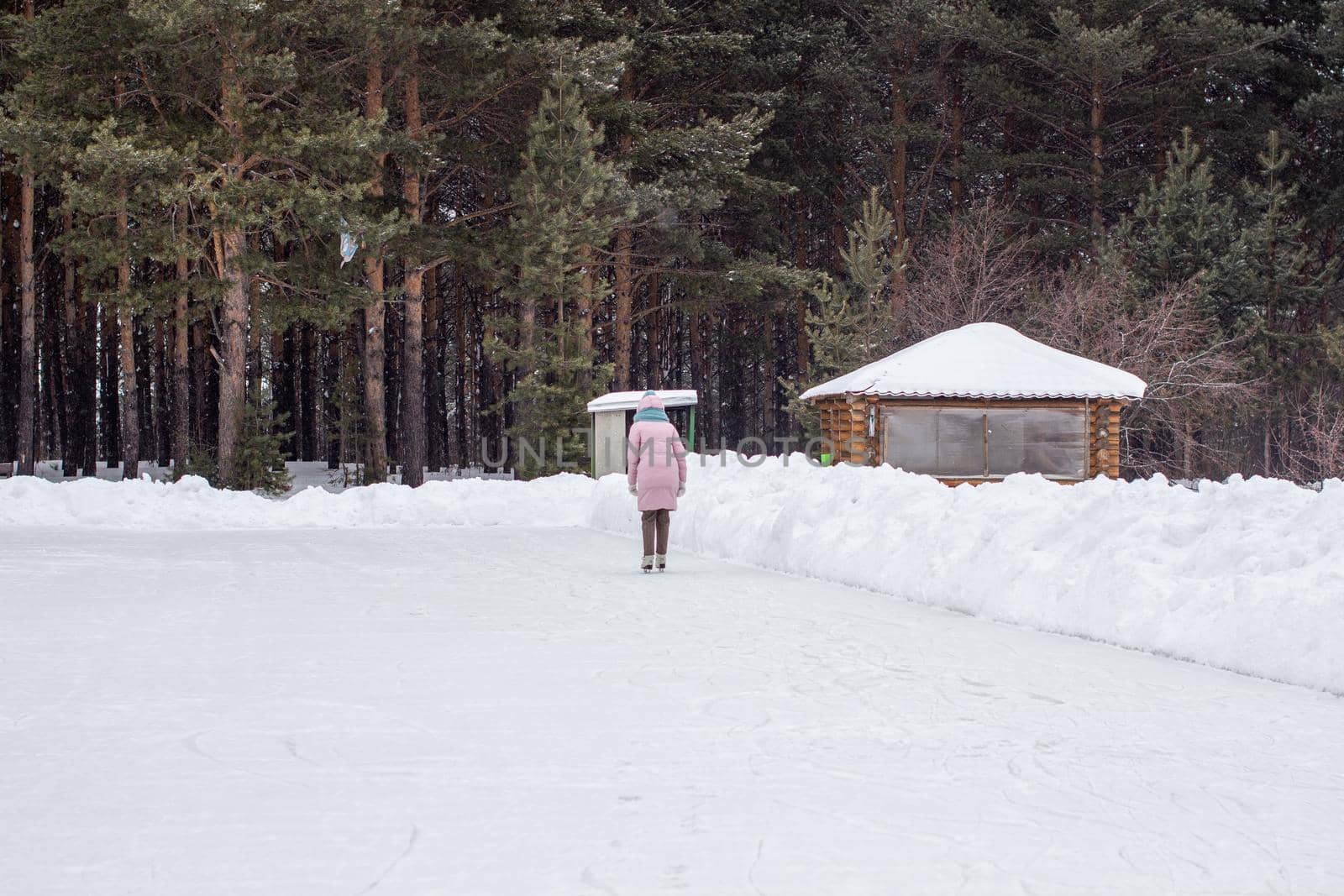 One girl in warm clothes rides on an ice rink near the forest.  by AnatoliiFoto