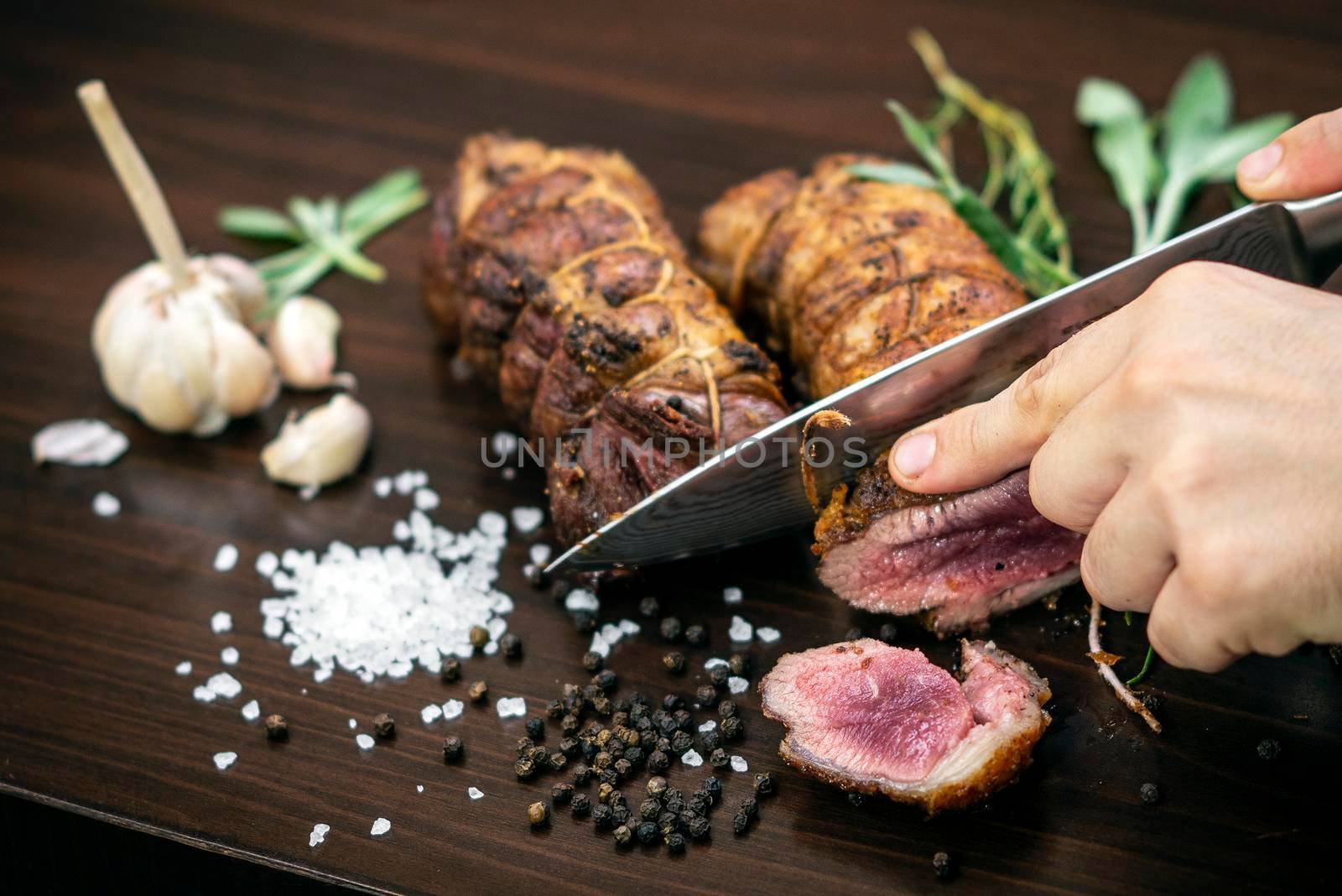 slicing a serving of organic roast beef roll with knife on wood table with garlic pepper and salt in melbourne australia