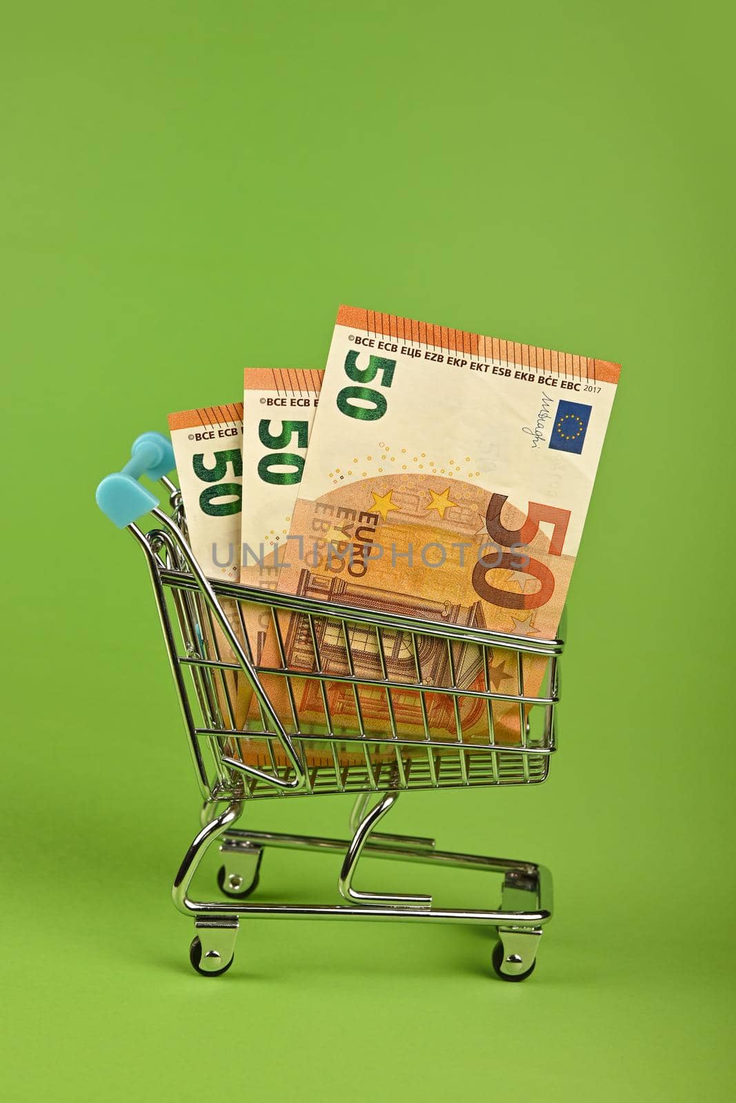 Close up several fifty Euro paper currency banknotes in small shopping cart over green background, low angle side view