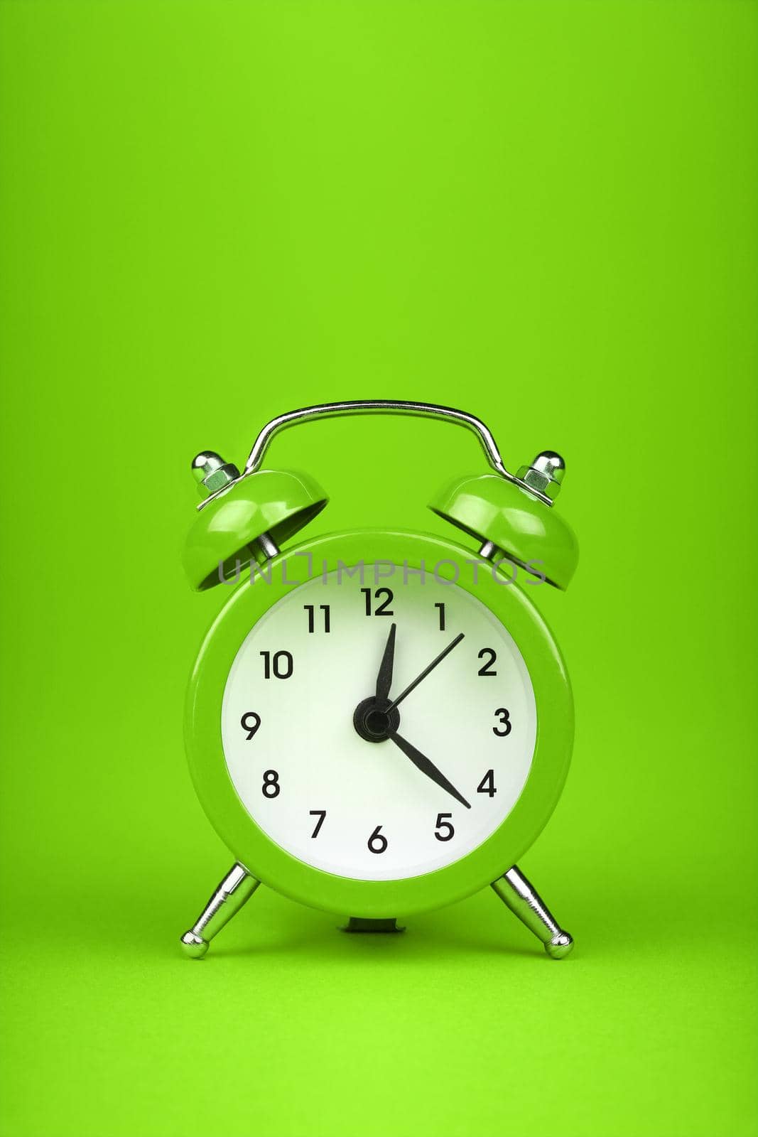 Close up one small green metal twin bell retro alarm clock over fresh green color paper background with copy space, low angle front view