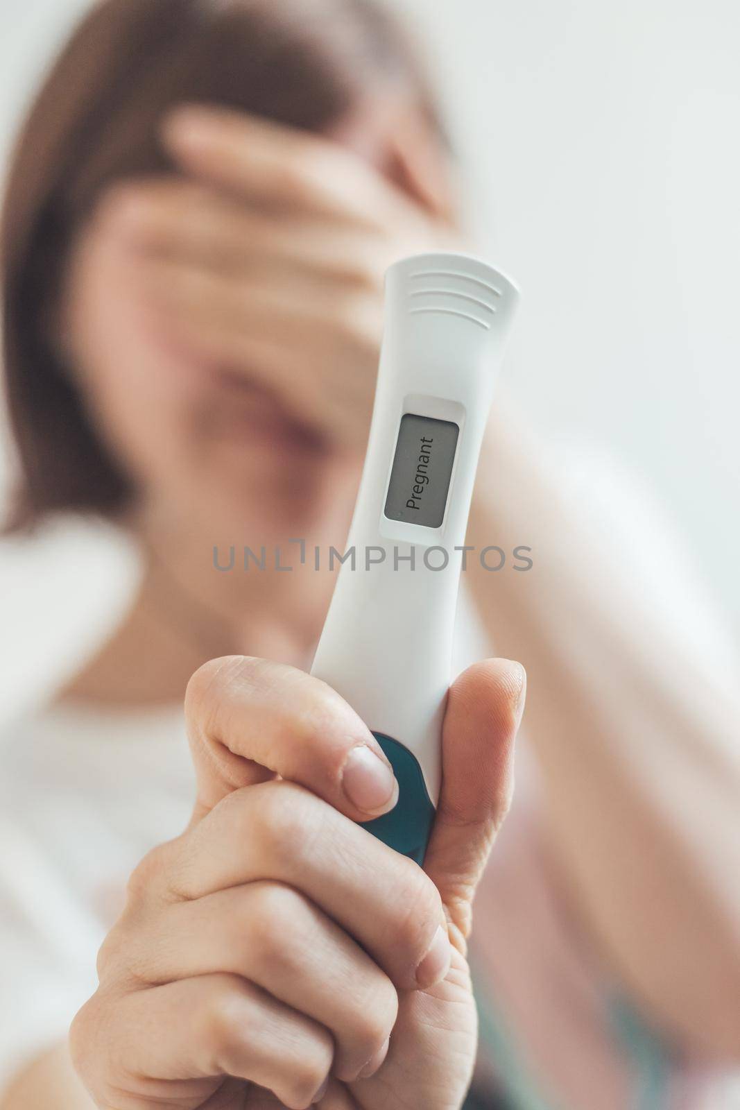 Nervous woman sitting on the bed, checking pregnancy test. Result positive, “Pregnant” by Daxenbichler